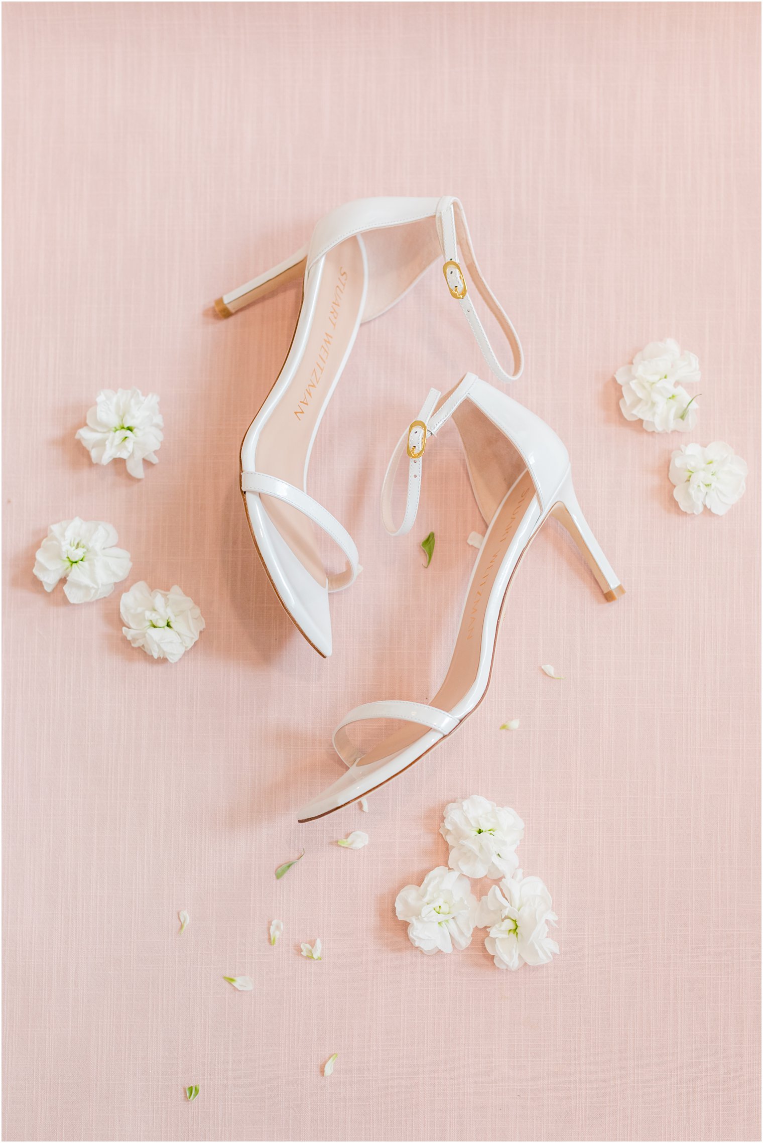 bride's white shoes rest on pink board with white flowers 