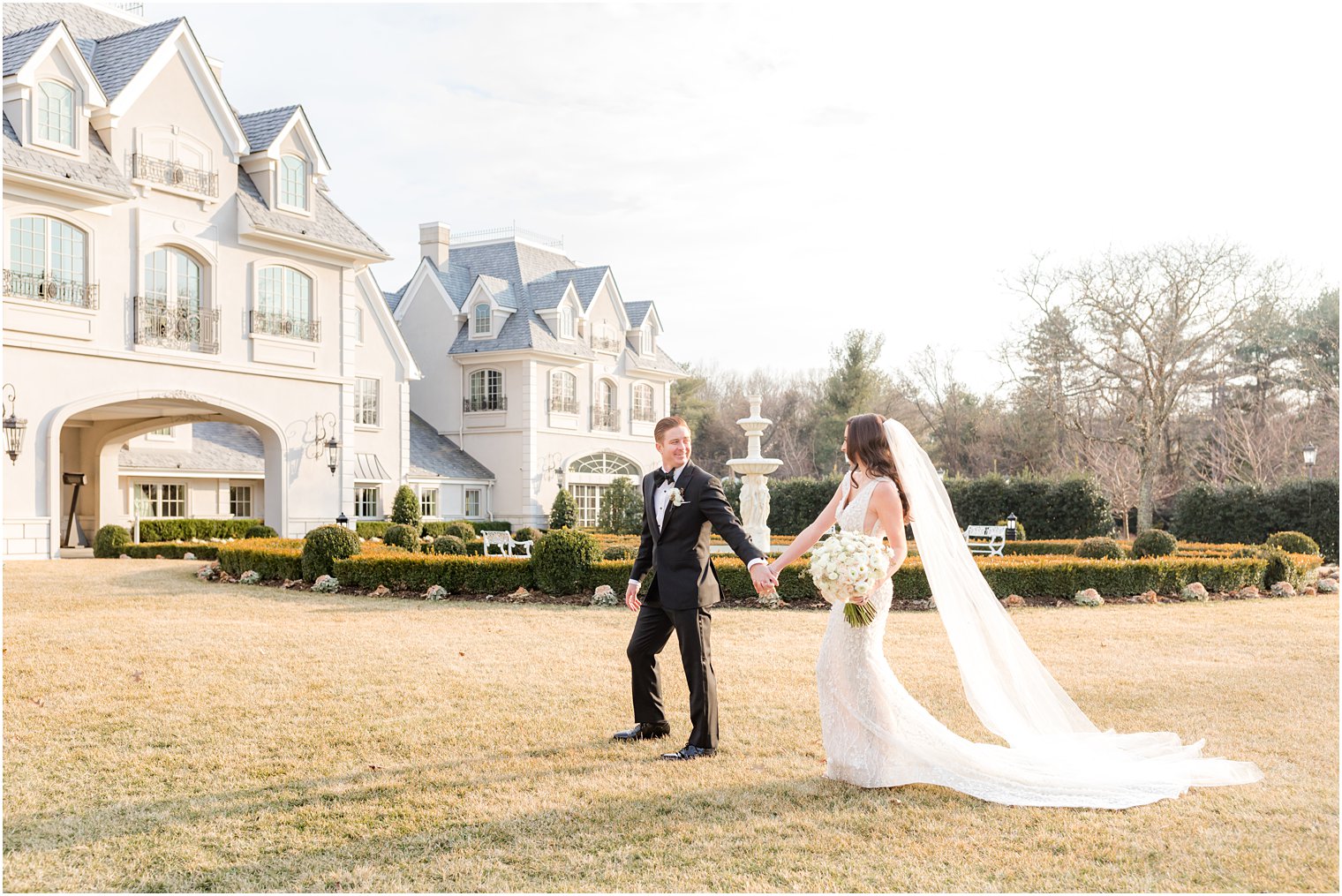 bride and groom hold hands walking on lawn before Park Chateau winter wedding