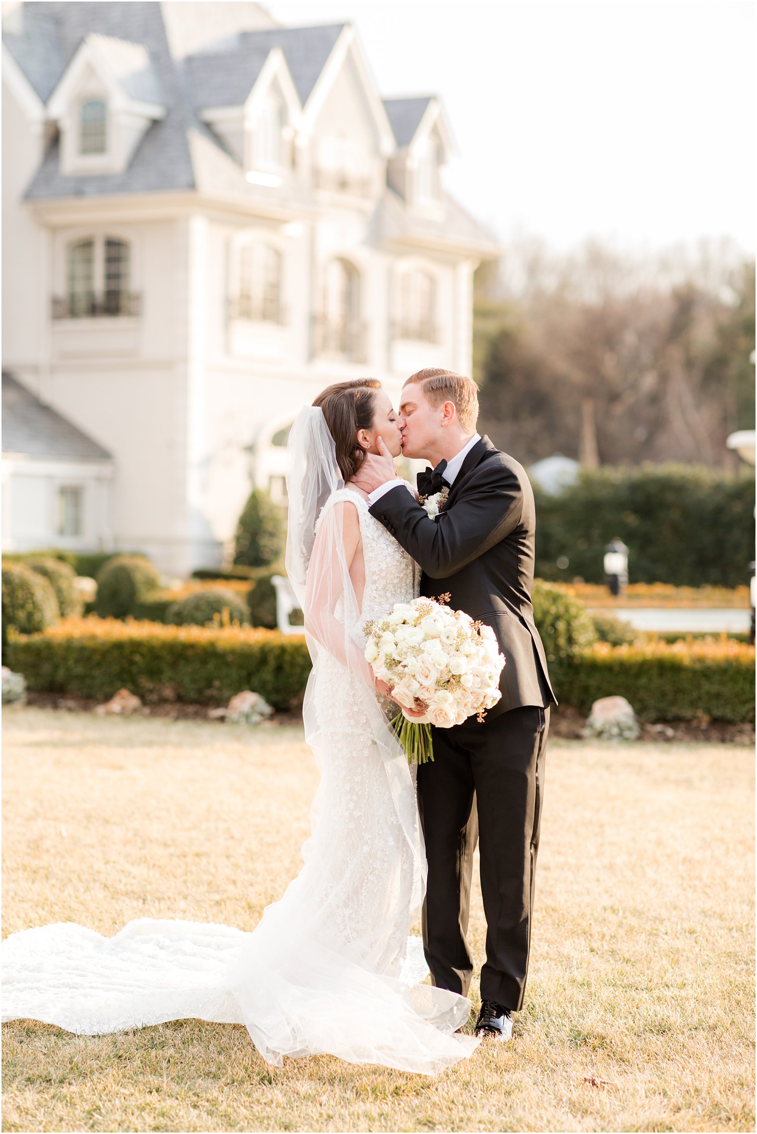 bride and groom kiss during New Jersey wedding portraits on front lawn of manor home 