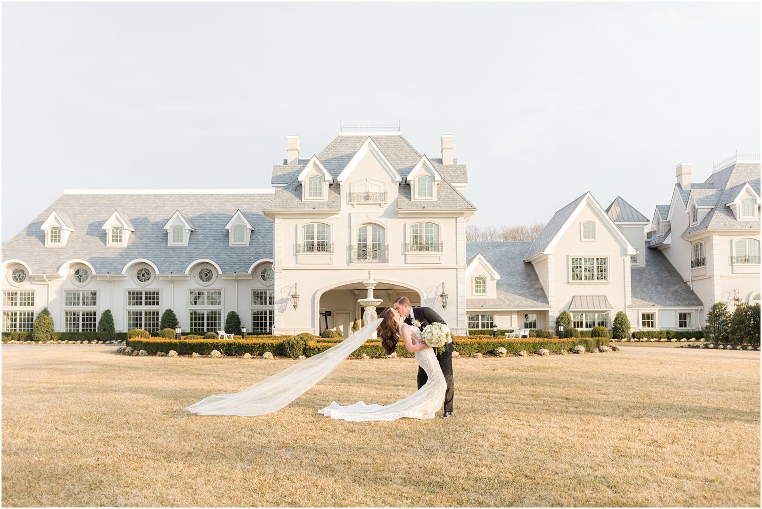 newlyweds kiss on lawn with bride's veil floating behind her 