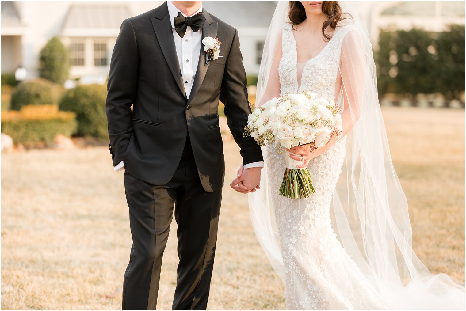 bride and groom hold hands while bride holds bouquet of pastel and white flowers 