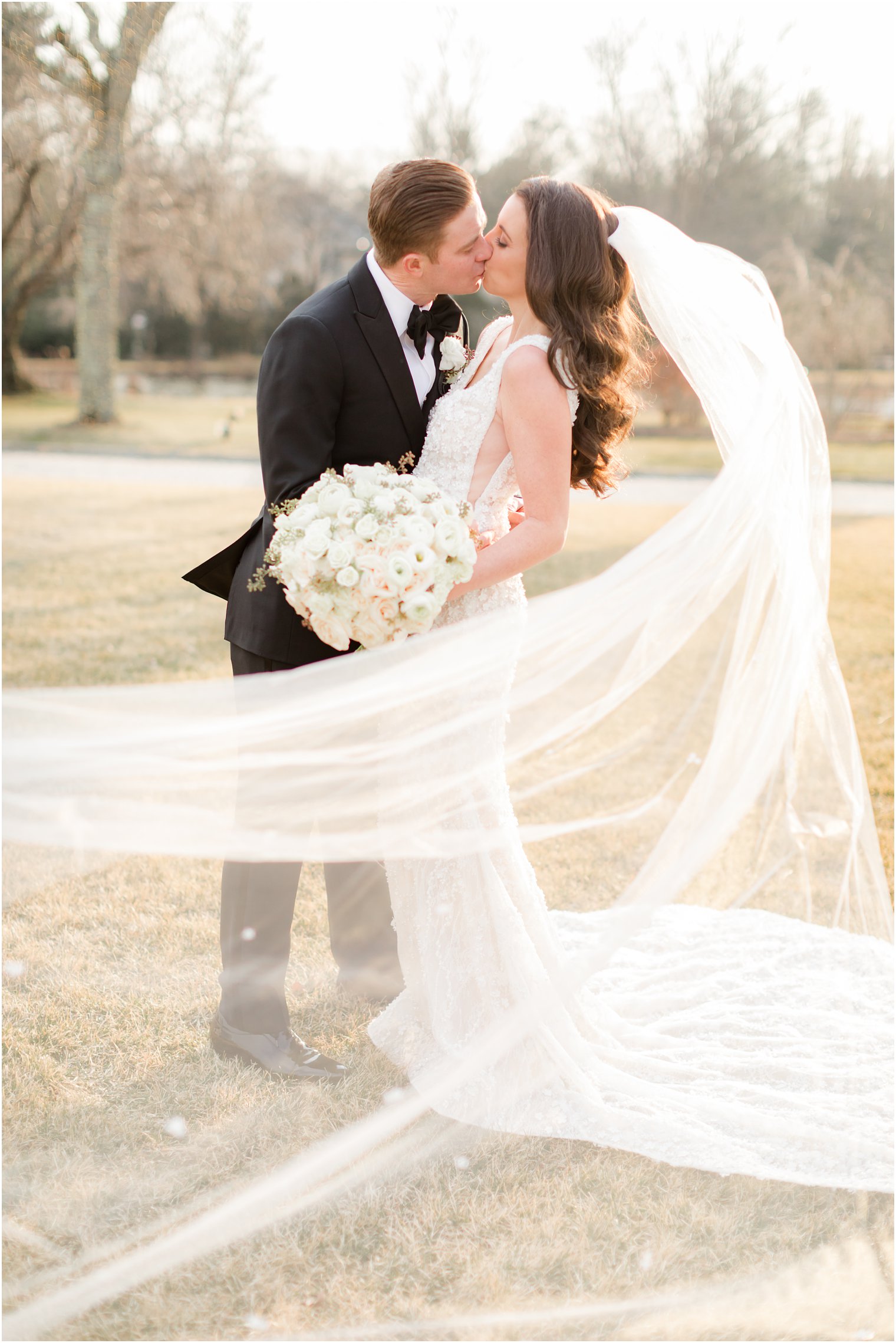 bride and groom kiss with bride's veil floating around them 