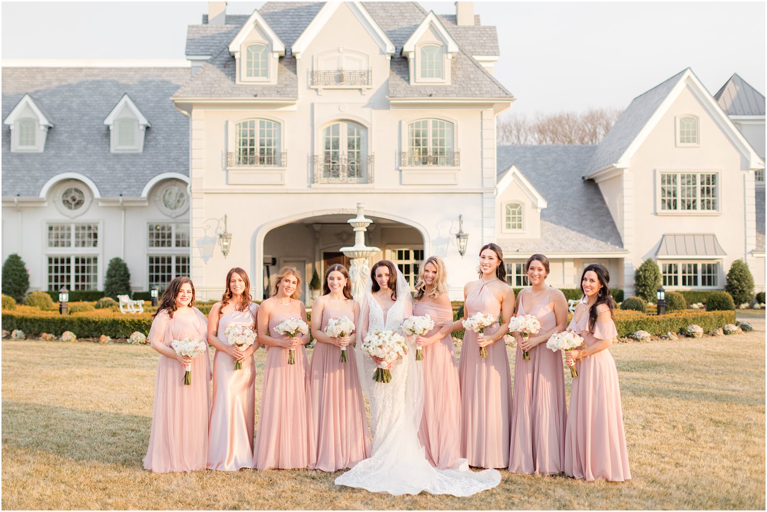 bride poses with bridesmaids in pastel pink gowns on lawn at Park Chateau Estate 
