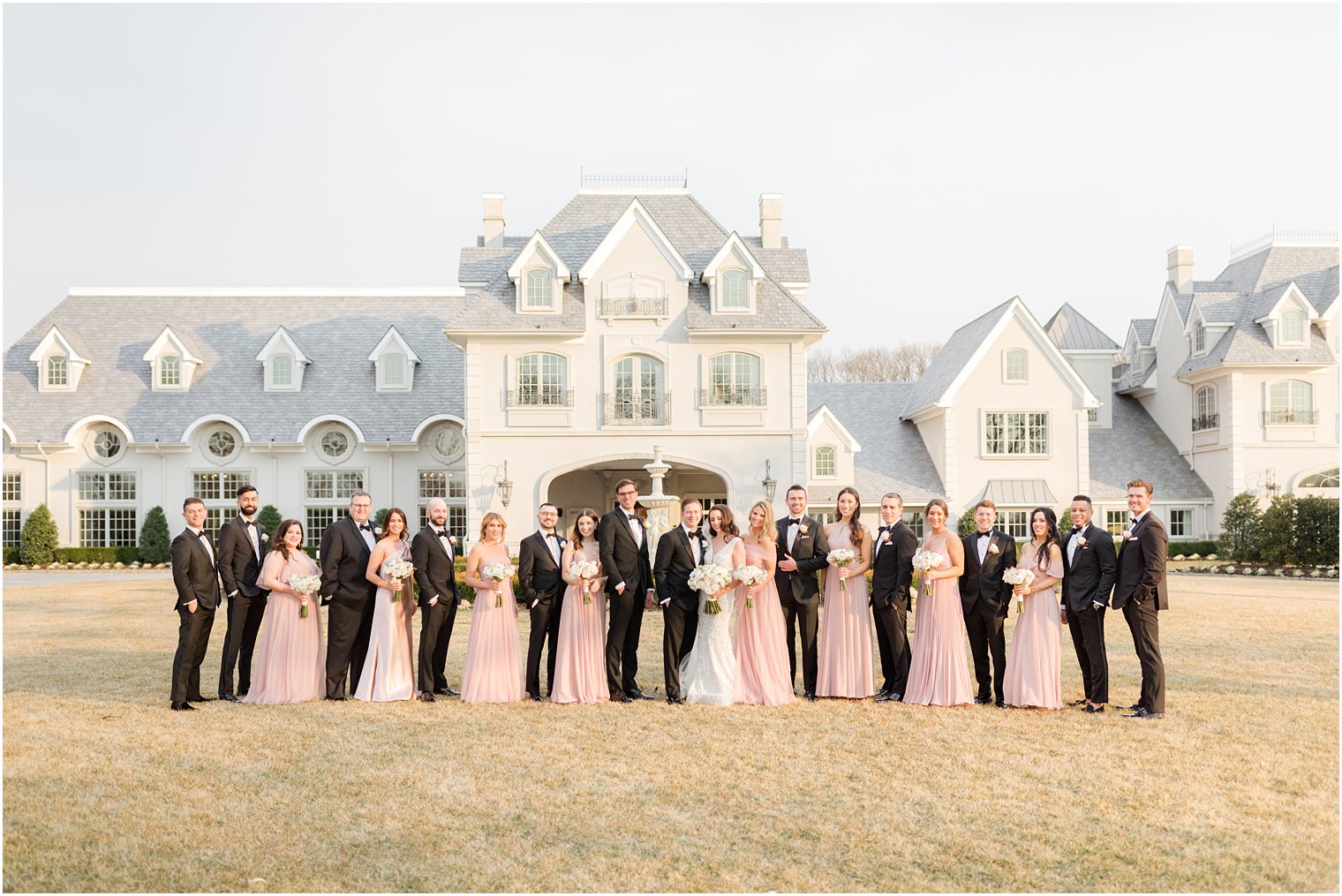bride and bridesmaids pose with entire wedding party in pink gowns and black tuxes 