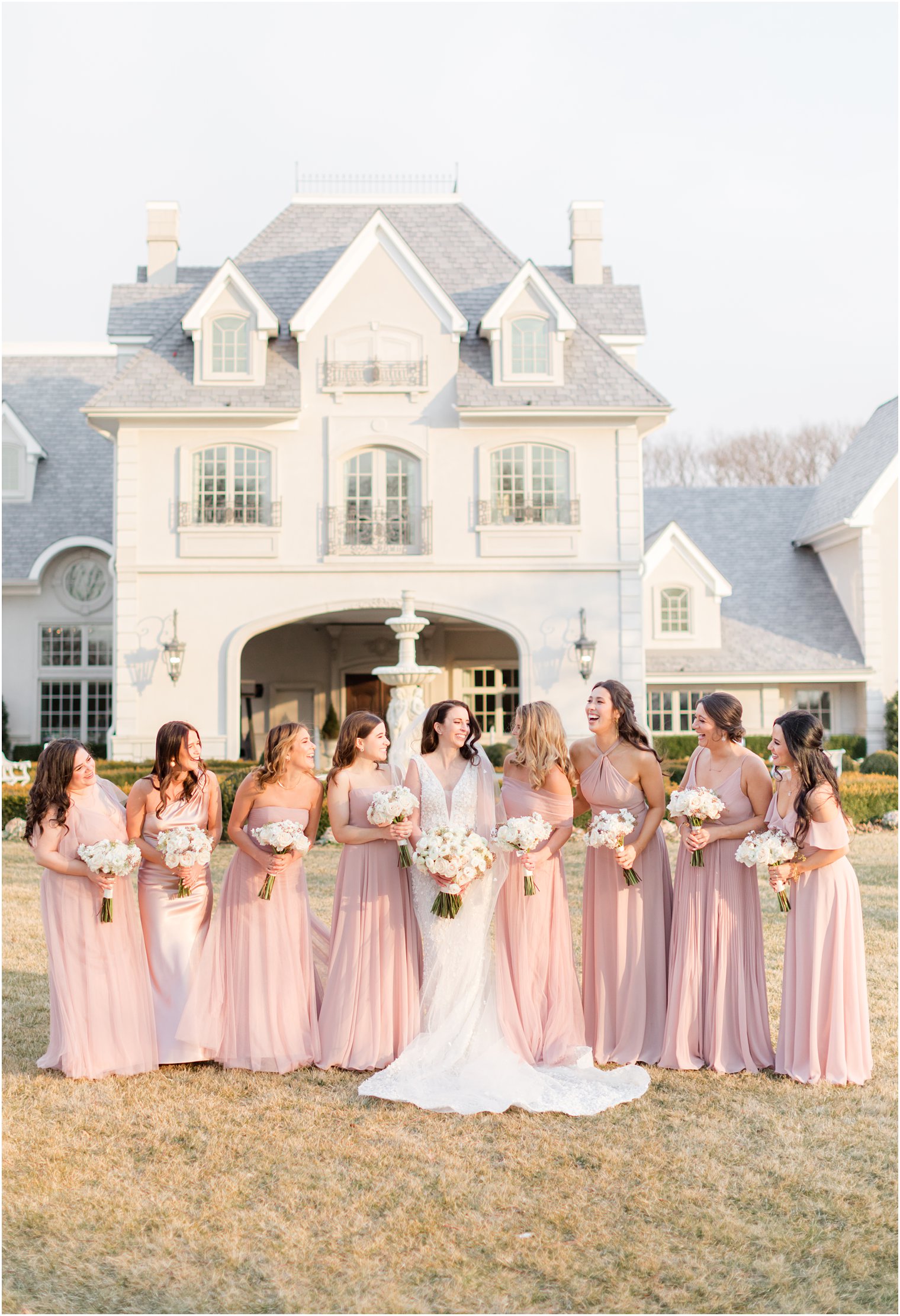 bride laughs with bridesmaids in pastel pink gowns on lawn at Park Chateau Estate 