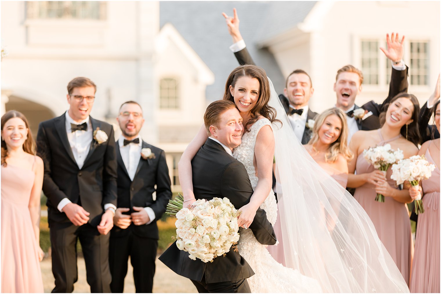 groom lifts up bride while wedding party cheers in New Jersey 
