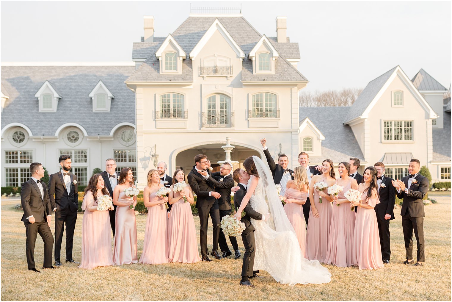 bride and groom kiss while wedding party cheers on lawn at Park Chateau Estate 