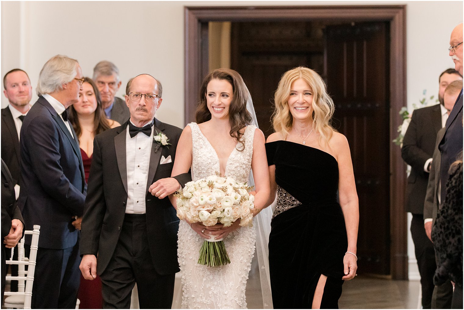 bride smiles walking down aisle with parents for Jewish wedding ceremony 