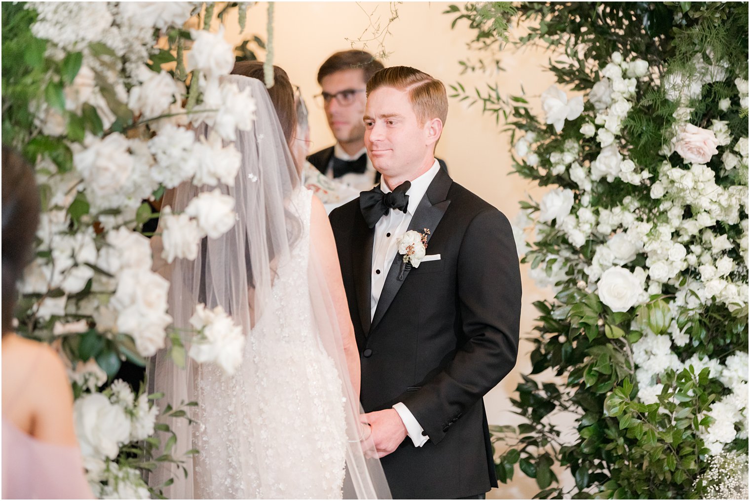 groom smiles at bride under floral canopy during wedding ceremony 