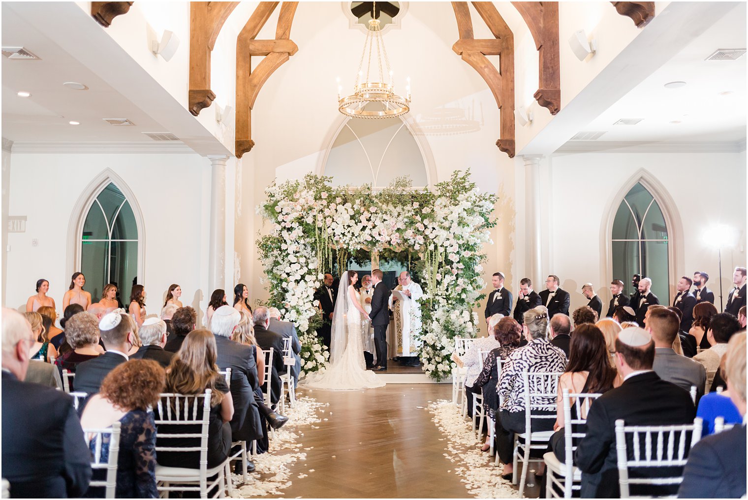 bride and groom hold hands under floral canopy for wedding ceremony at Park Chateau 