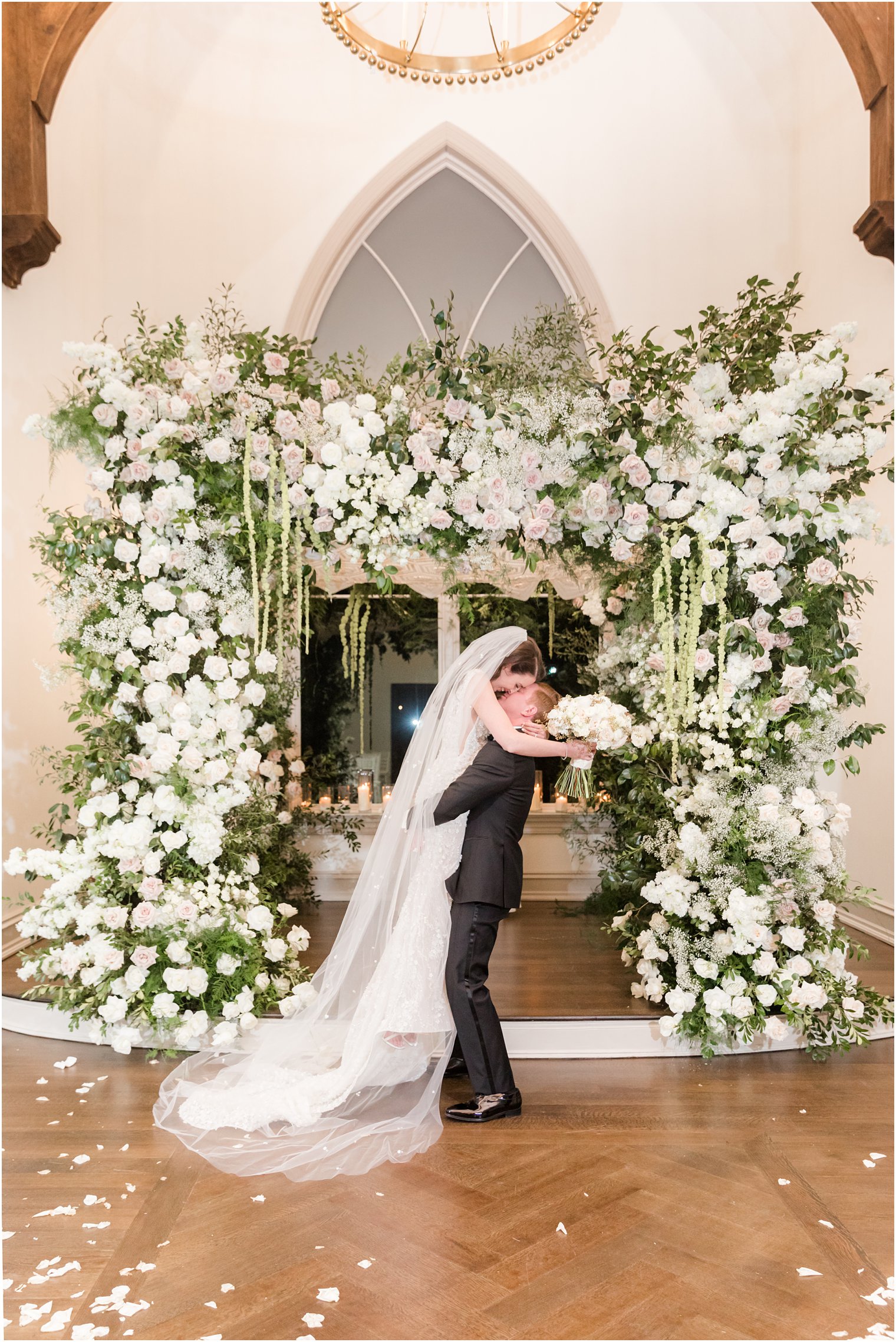 groom lifts bride in front of floral canopy in Park Chateau Estate chapel 