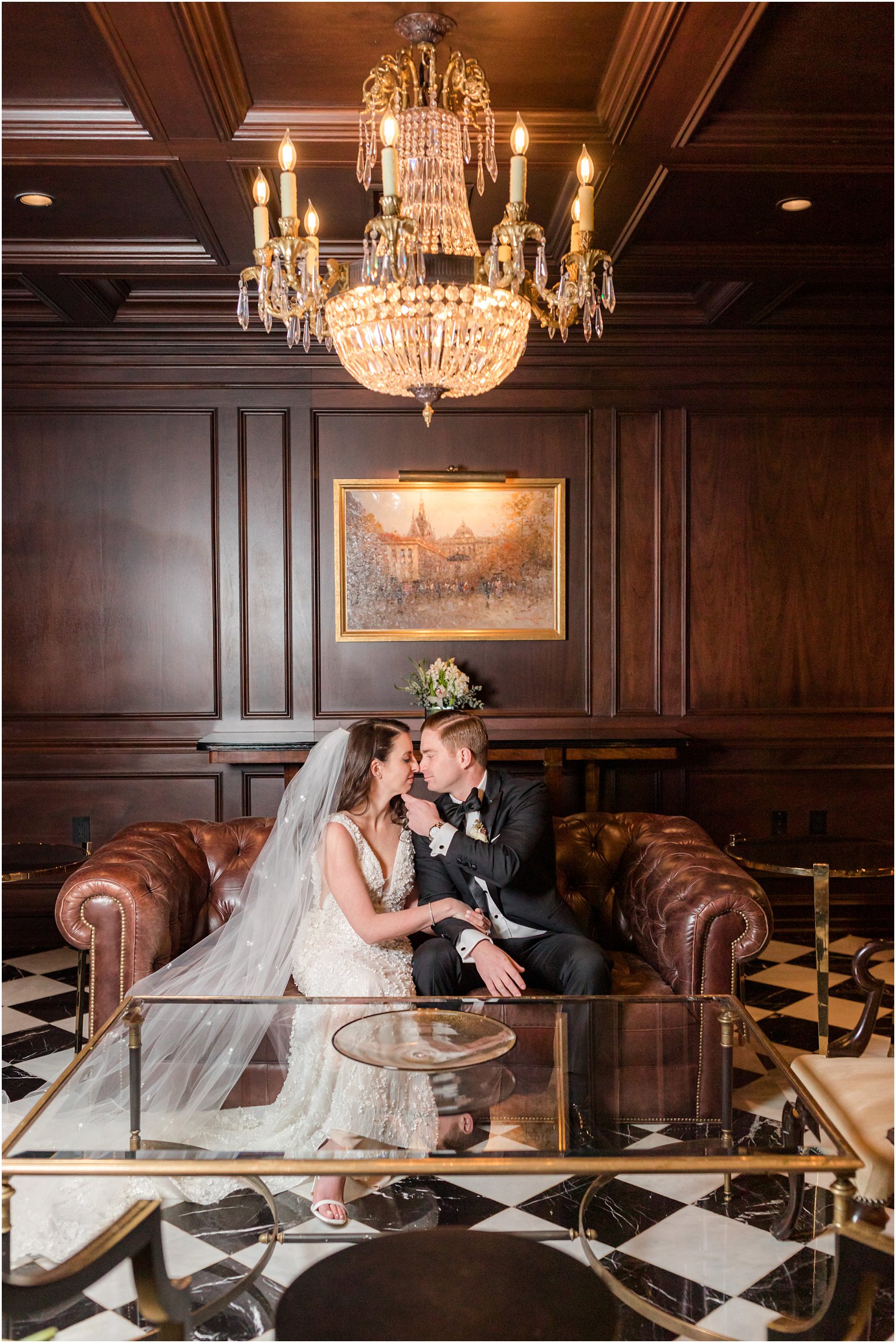 bride and groom sit on leather couch nuzzling noses 