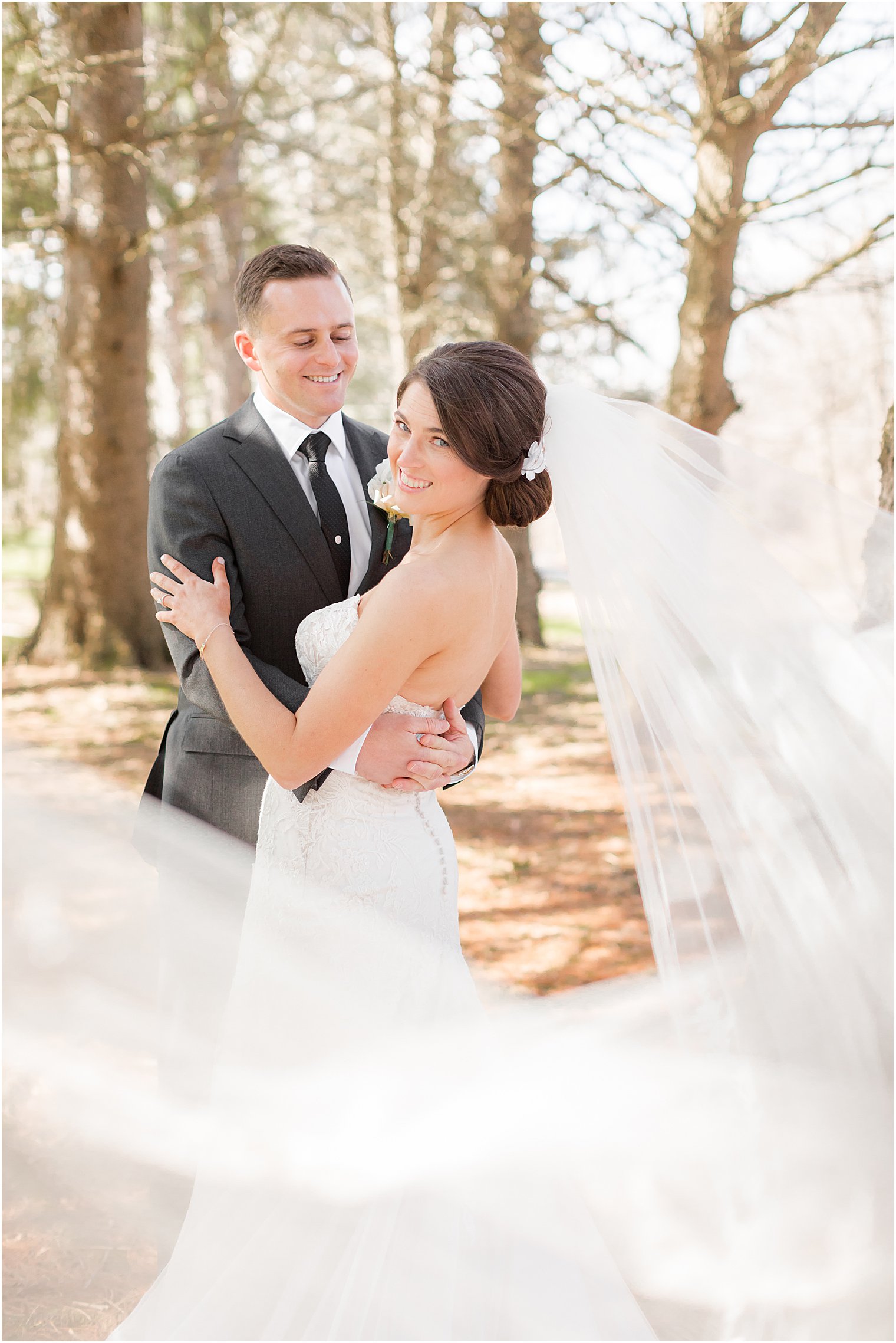 groom smiles at bride with veil flowing behind her