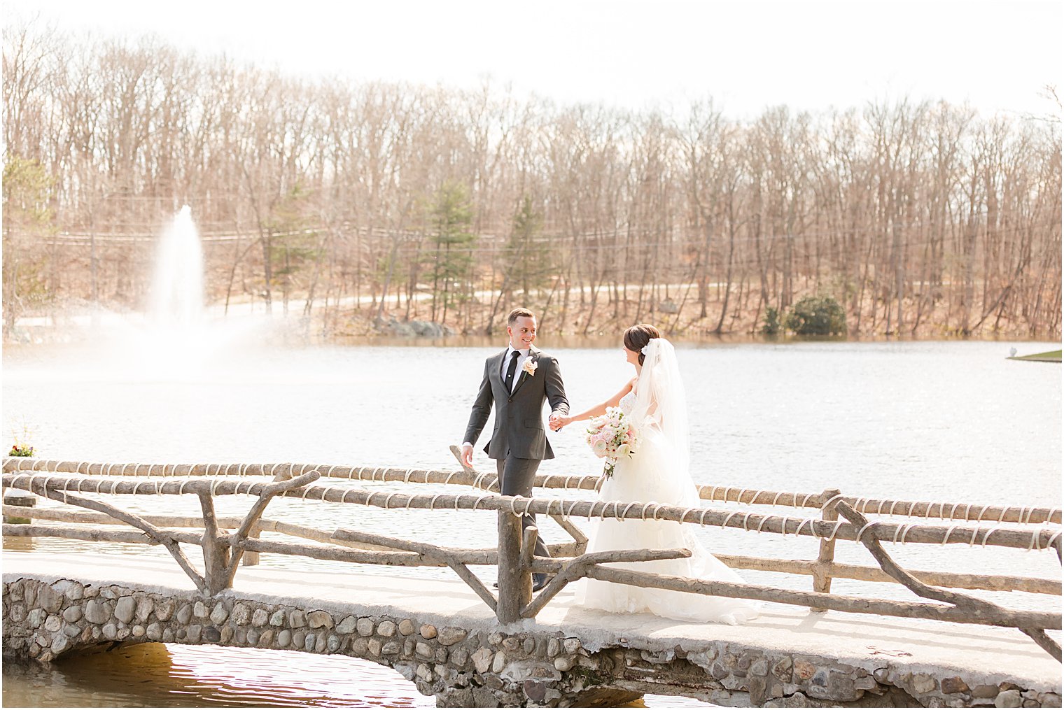 couple walks over wooden bridge on lake at The Refinery at Perona Farms