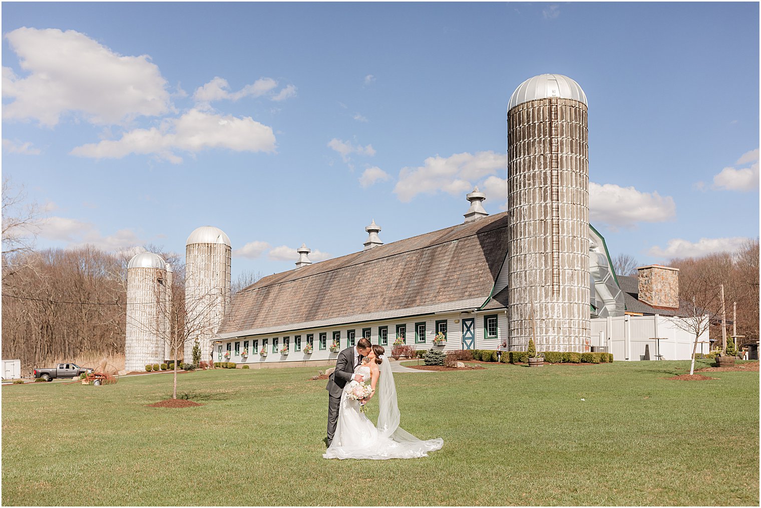 couple poses in front of farm house at The Refinery at Perona Farms