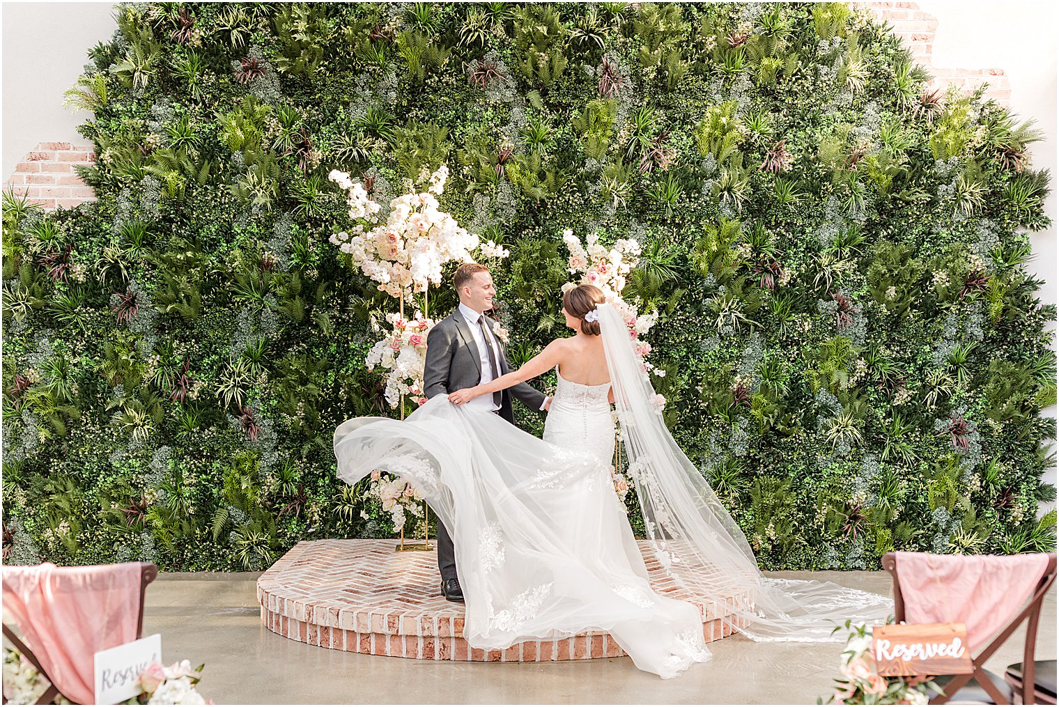 bride twirls gown in front of greenery wall at The Refinery at Perona Farms