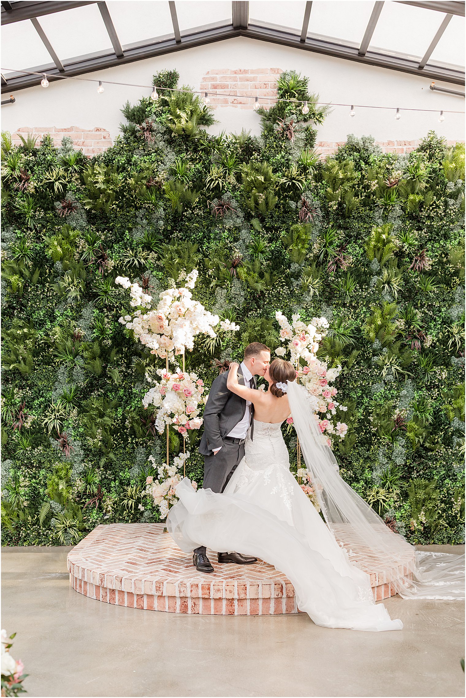 couple kisses by greenery wall and floral display