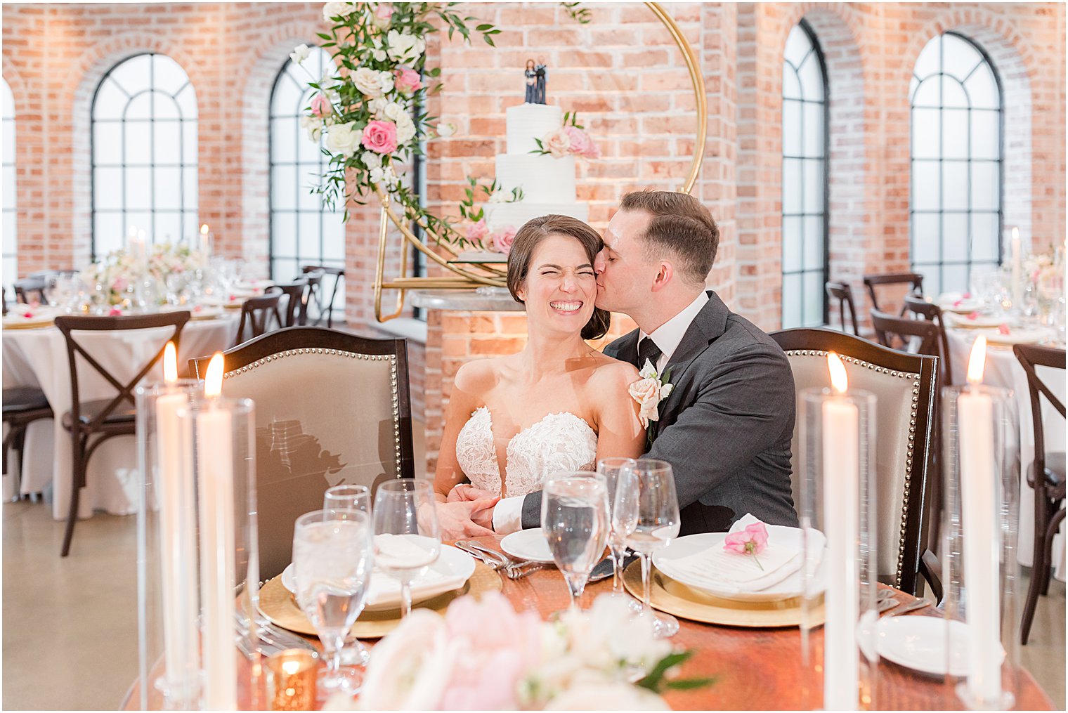 groom kisses bride's cheek during wedding portraits in reception hall at The Refinery at Perona Farms