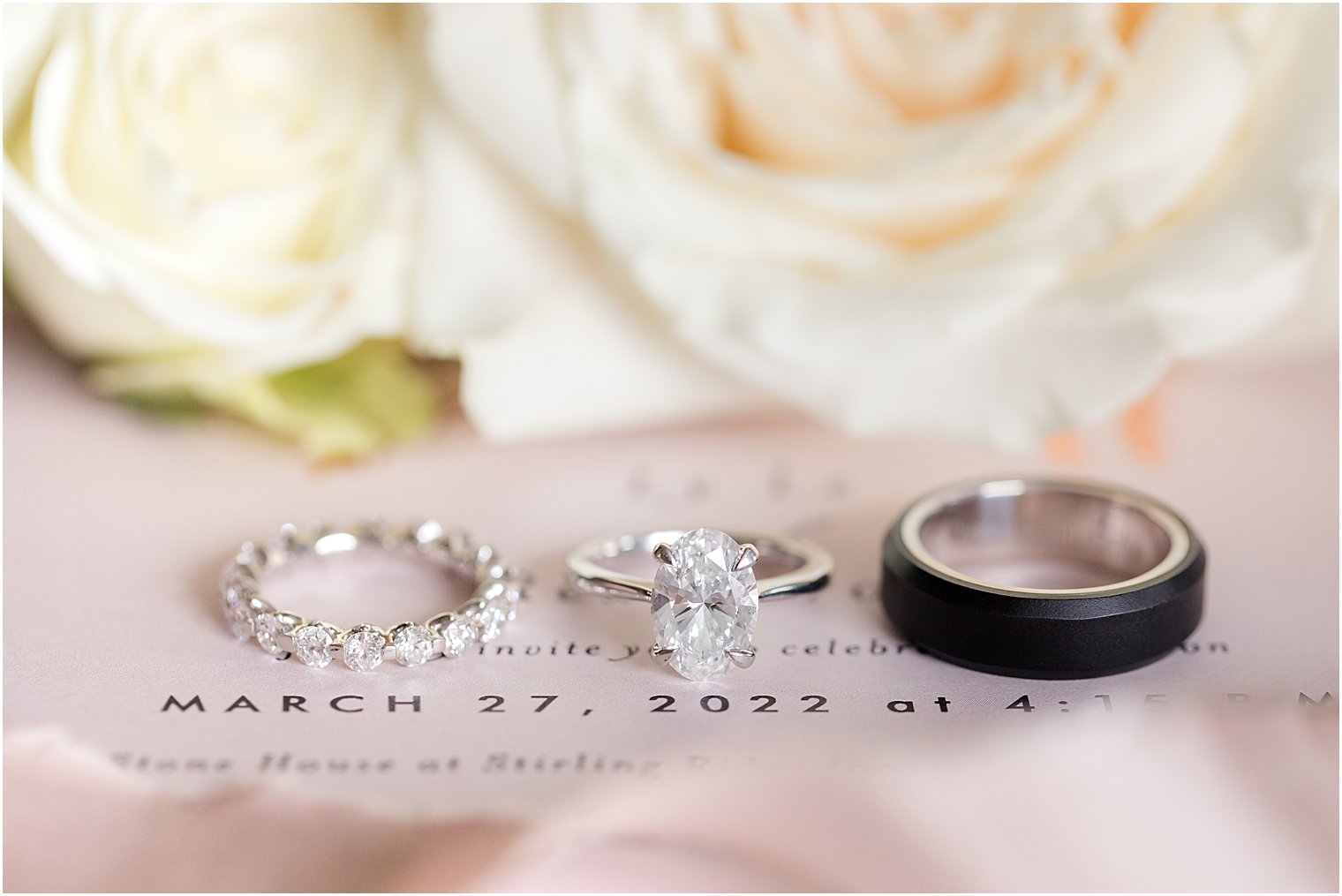 wedding bands rest on invitation suite in front of ivory flowers