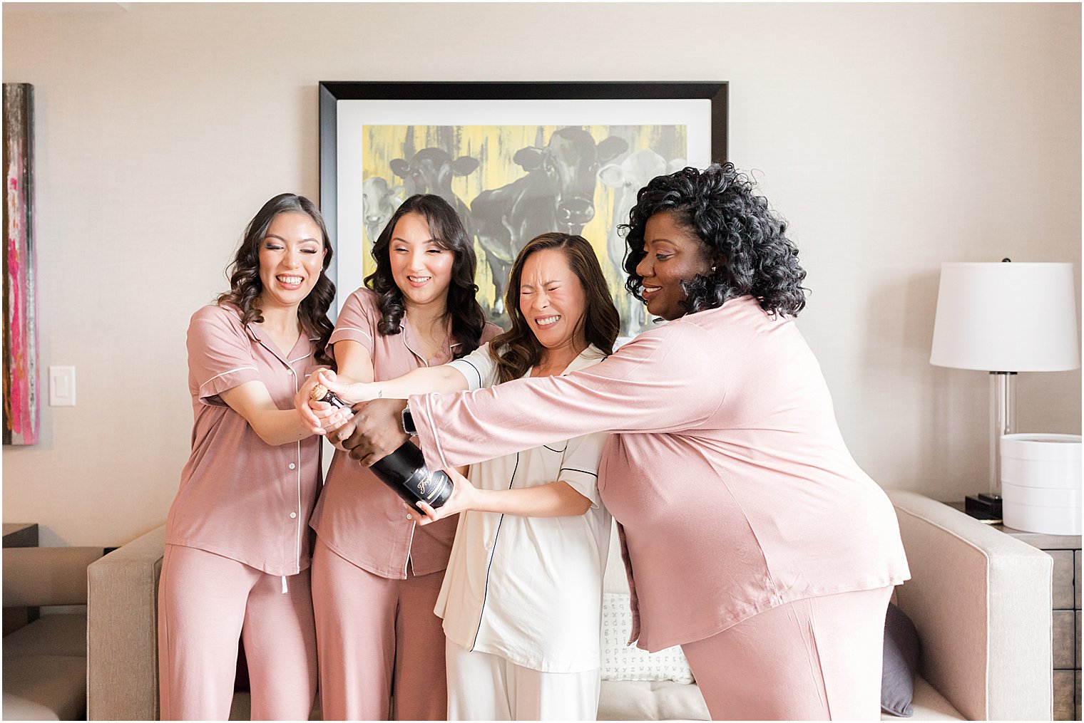 bride and bridesmaids pop bottle of champagne in matching pink pajamas