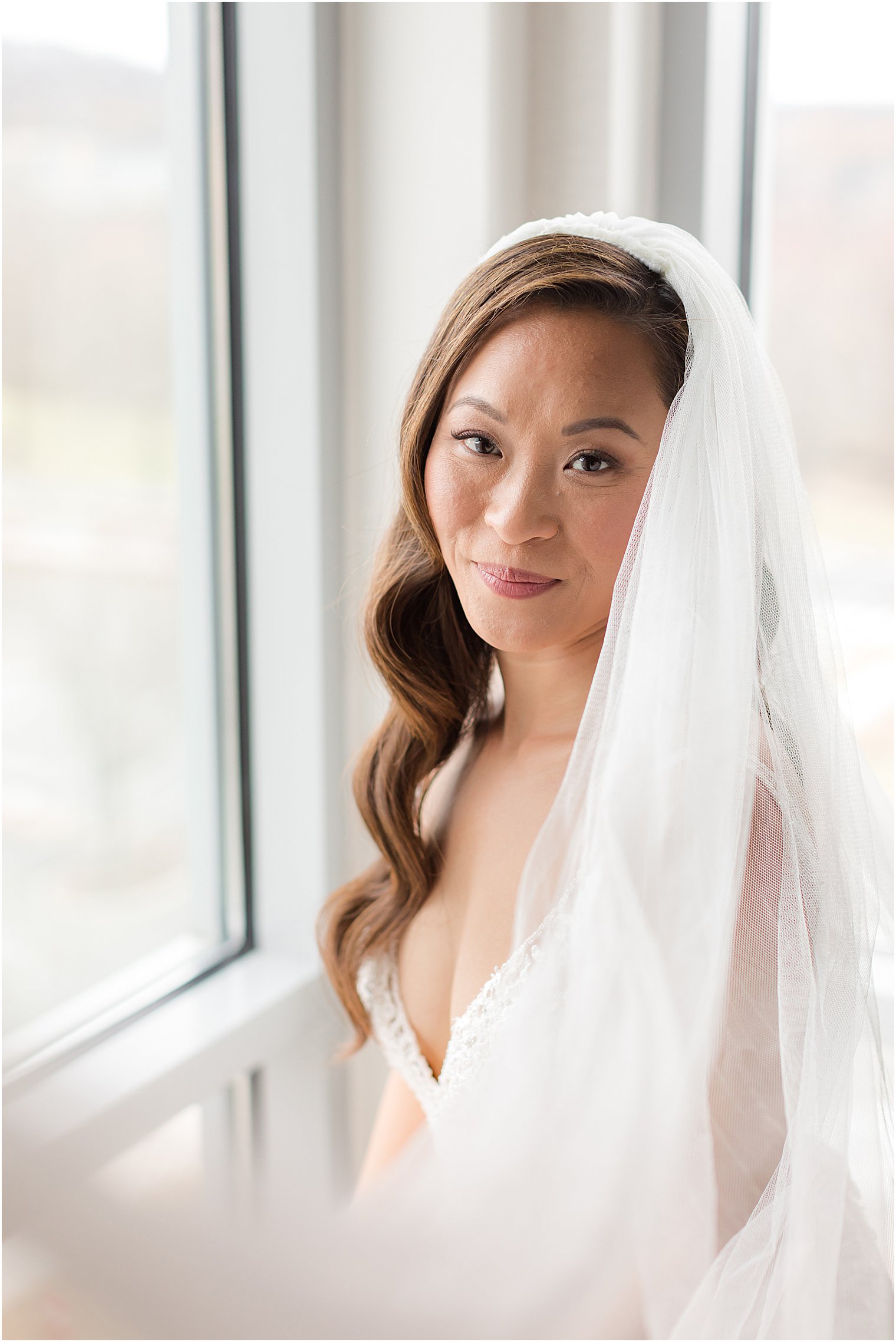 bride sits in window with veil around shoulders