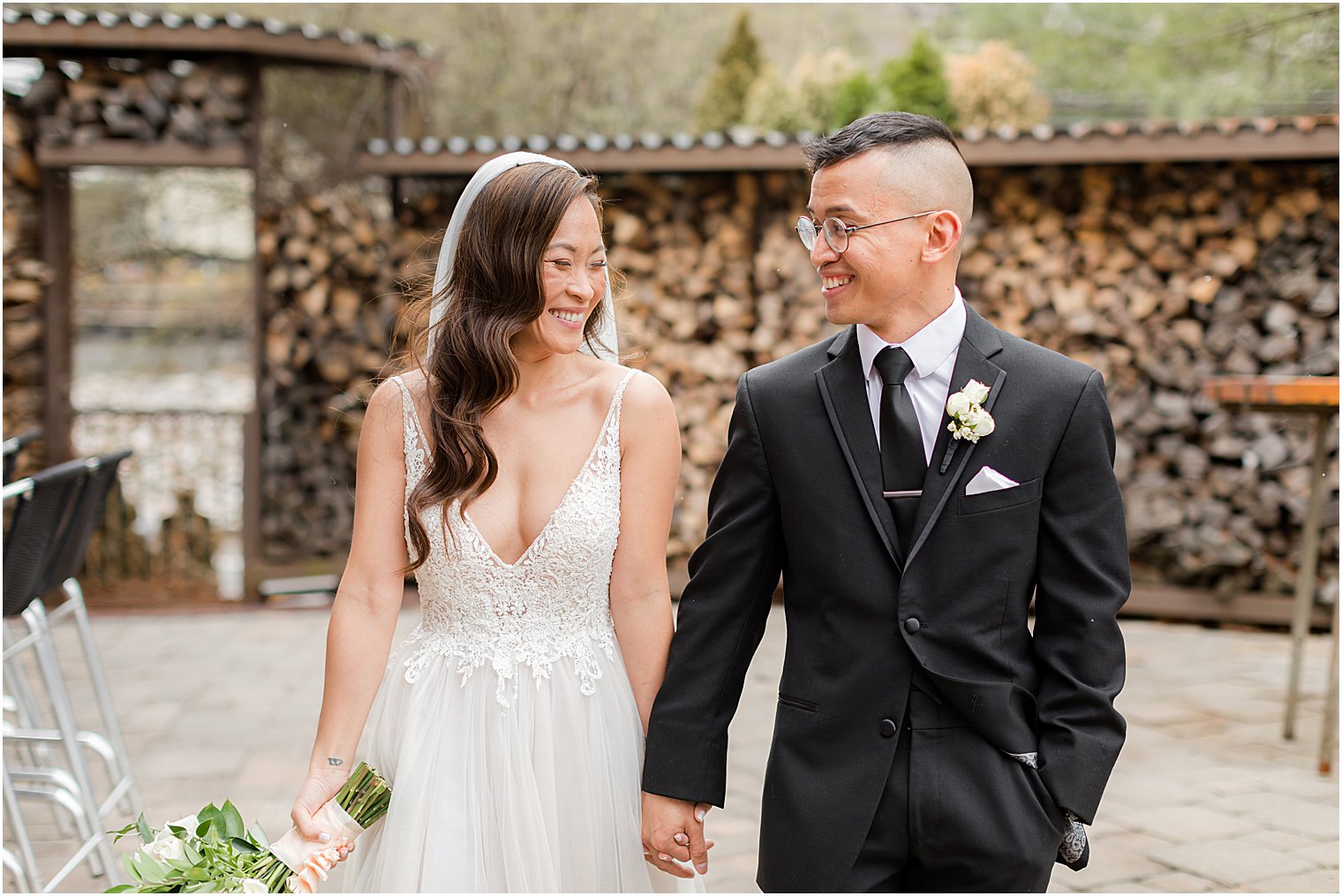 bride and groom hold hands walking by woodpile at The Lodge at Stirling Ridge