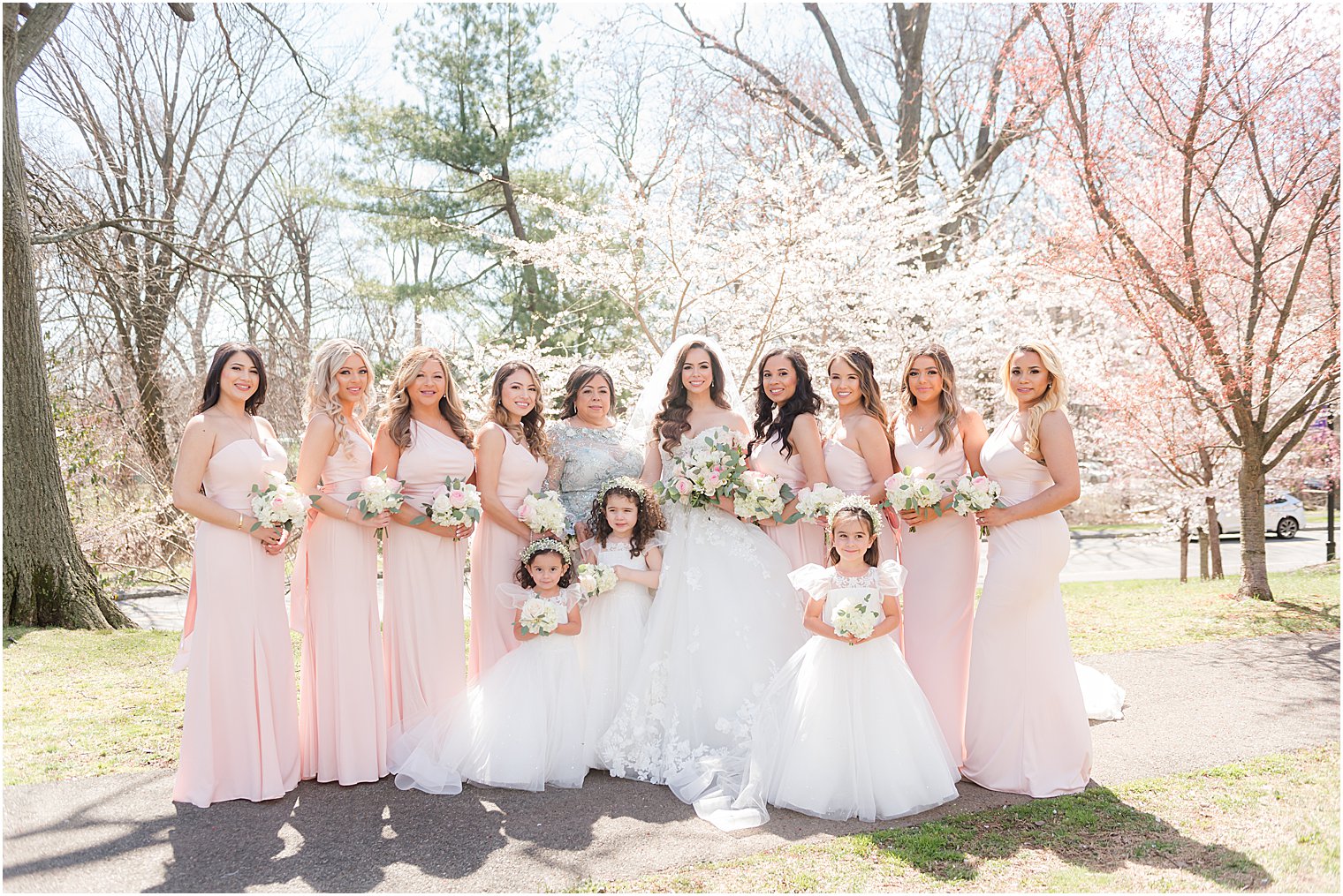 bride poses with bridesmaids in pink gowns by cherry blossoms