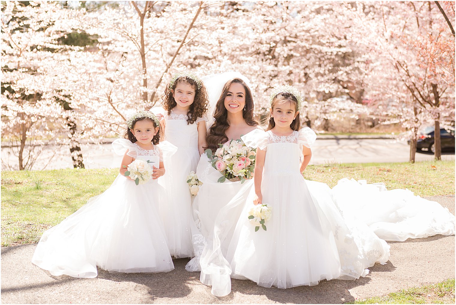 bride poses with three flower girls by cherry blossoms in Newark NJ