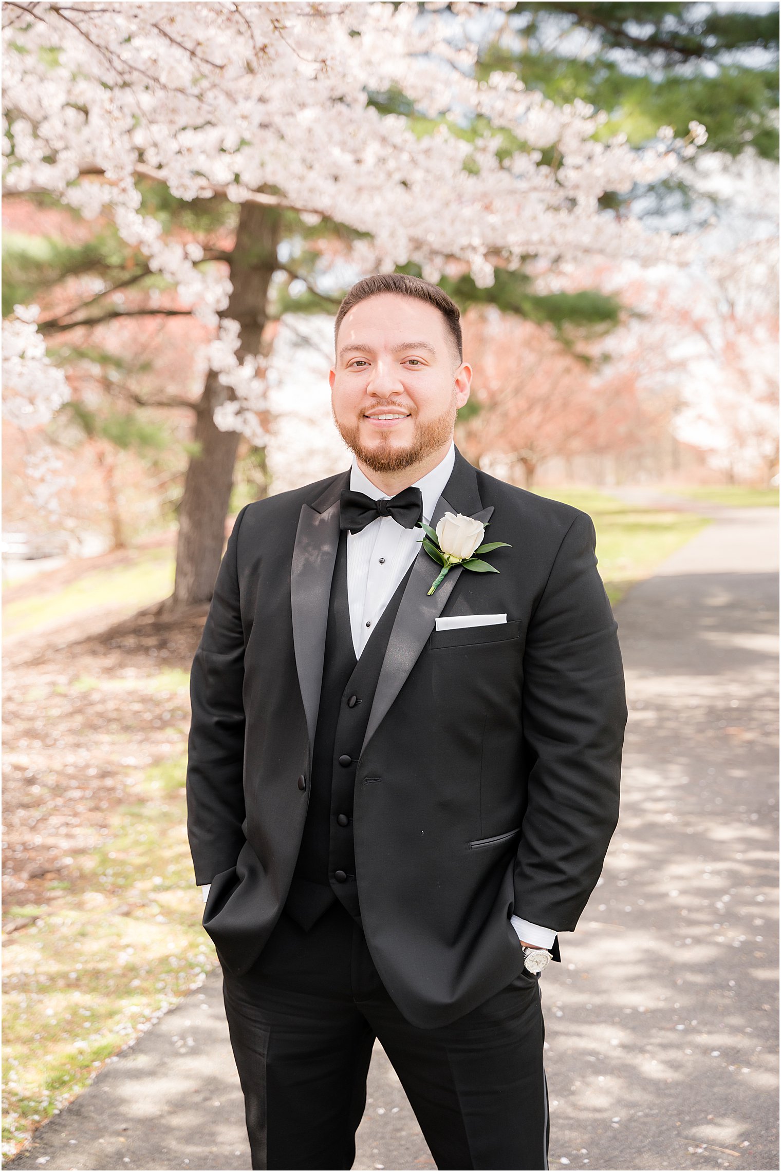 groom poses in classic tux by cherry blossoms
