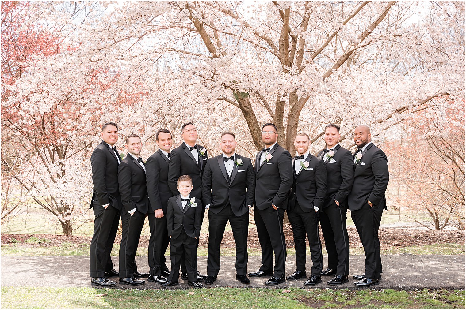 groom stands by groomsmen under cherry blossoms trees