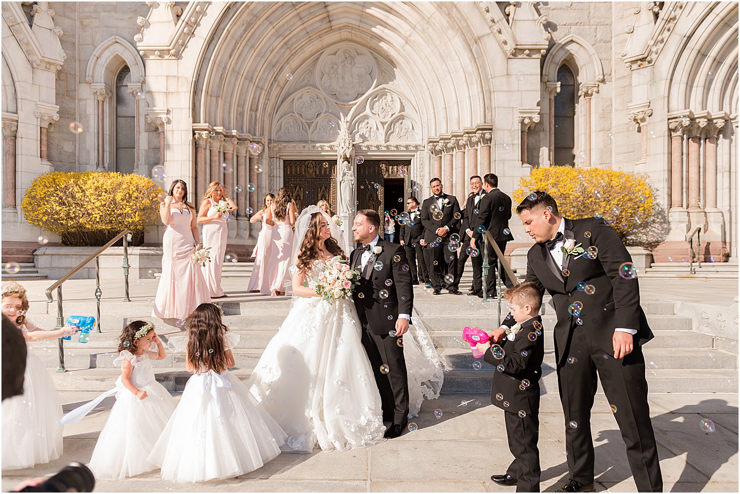 newlyweds stand with wedding party around them with bubbles outside the Cathedral Basilica of the Sacred Heart