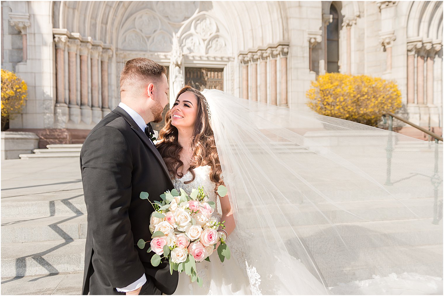 bride smiles up at groom with veil floating outside the Cathedral Basilica of the Sacred Heart