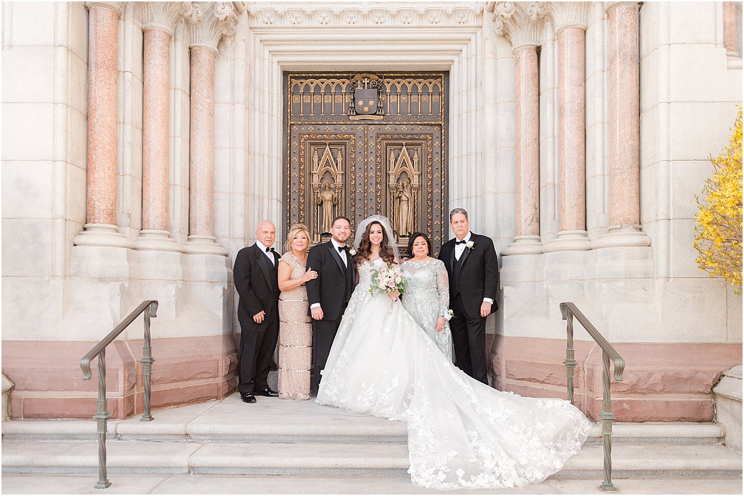 bride and groom stand on steps of the Cathedral Basilica of the Sacred Heart with parents 