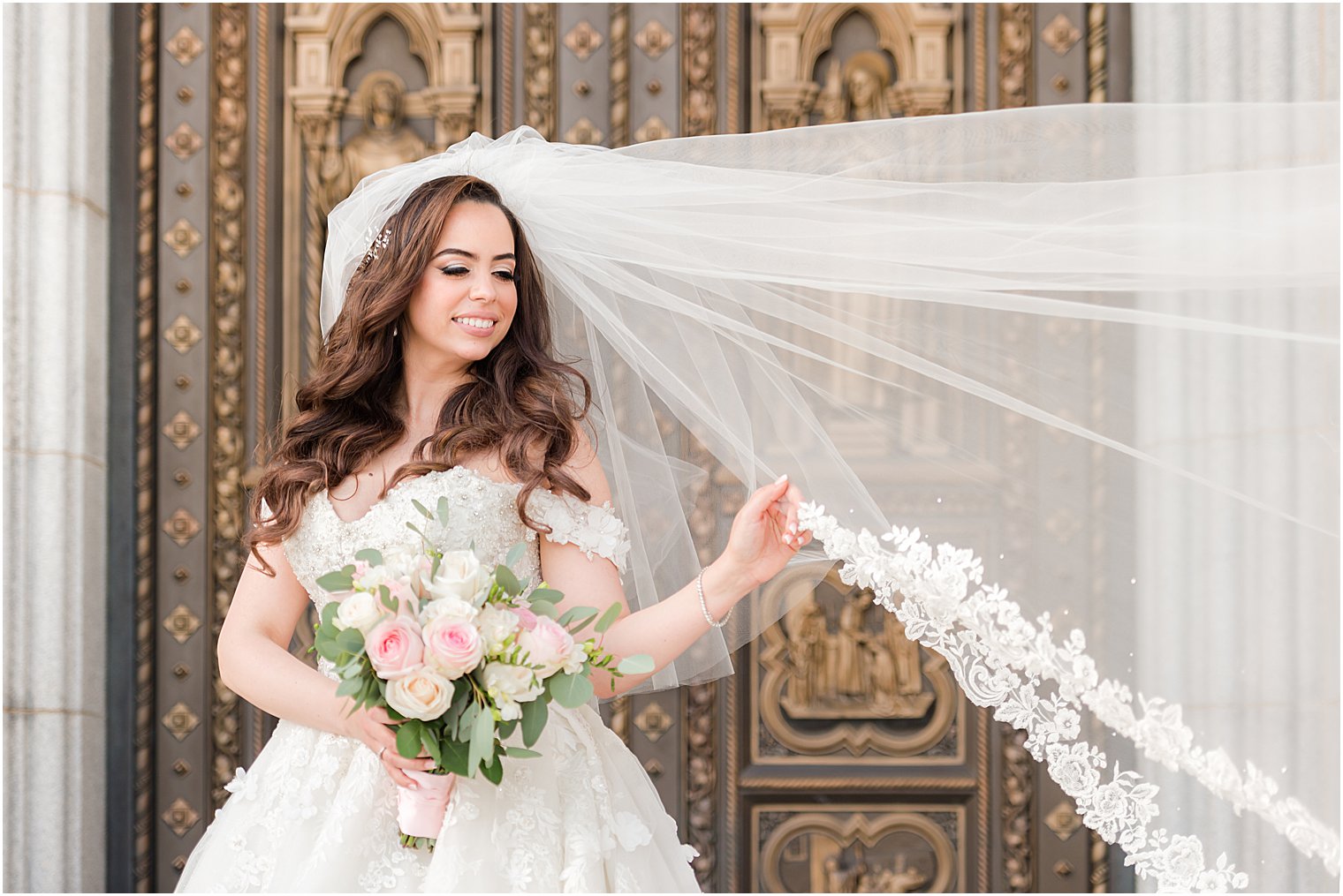 bride poses with veil floating outside doors of the Cathedral Basilica of the Sacred Heart