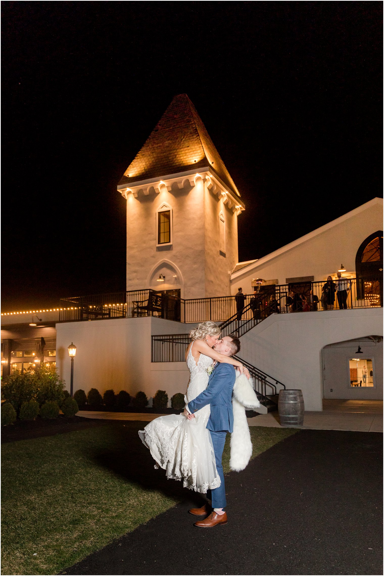 groom lifting bride at night in front of rustic wedding reception in Vineyard Ballroom at Renault Winery South Jersey Venue in Egg Harbor Township NJ