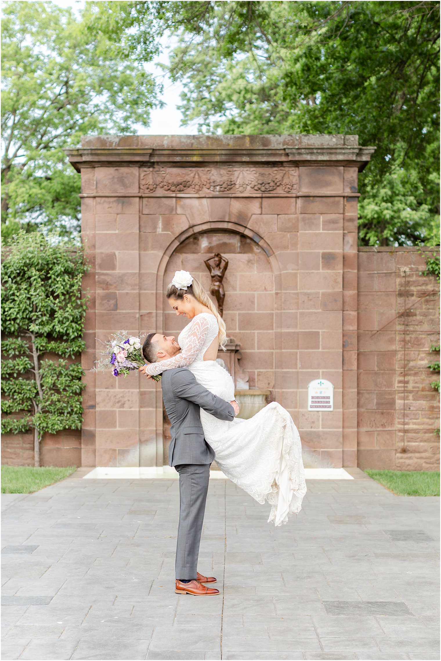 groom lifts bride up in front of brick fountain at Tyler Gardens