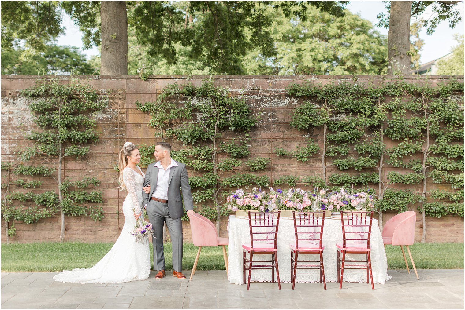 bride and groom stand by pink chairs and reception table with pink and purple flowers 