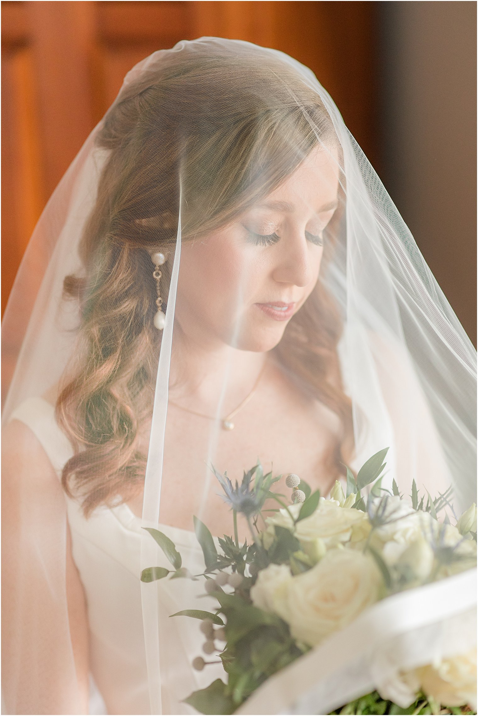 bride looks down at bouquet with veil over her shoulders 