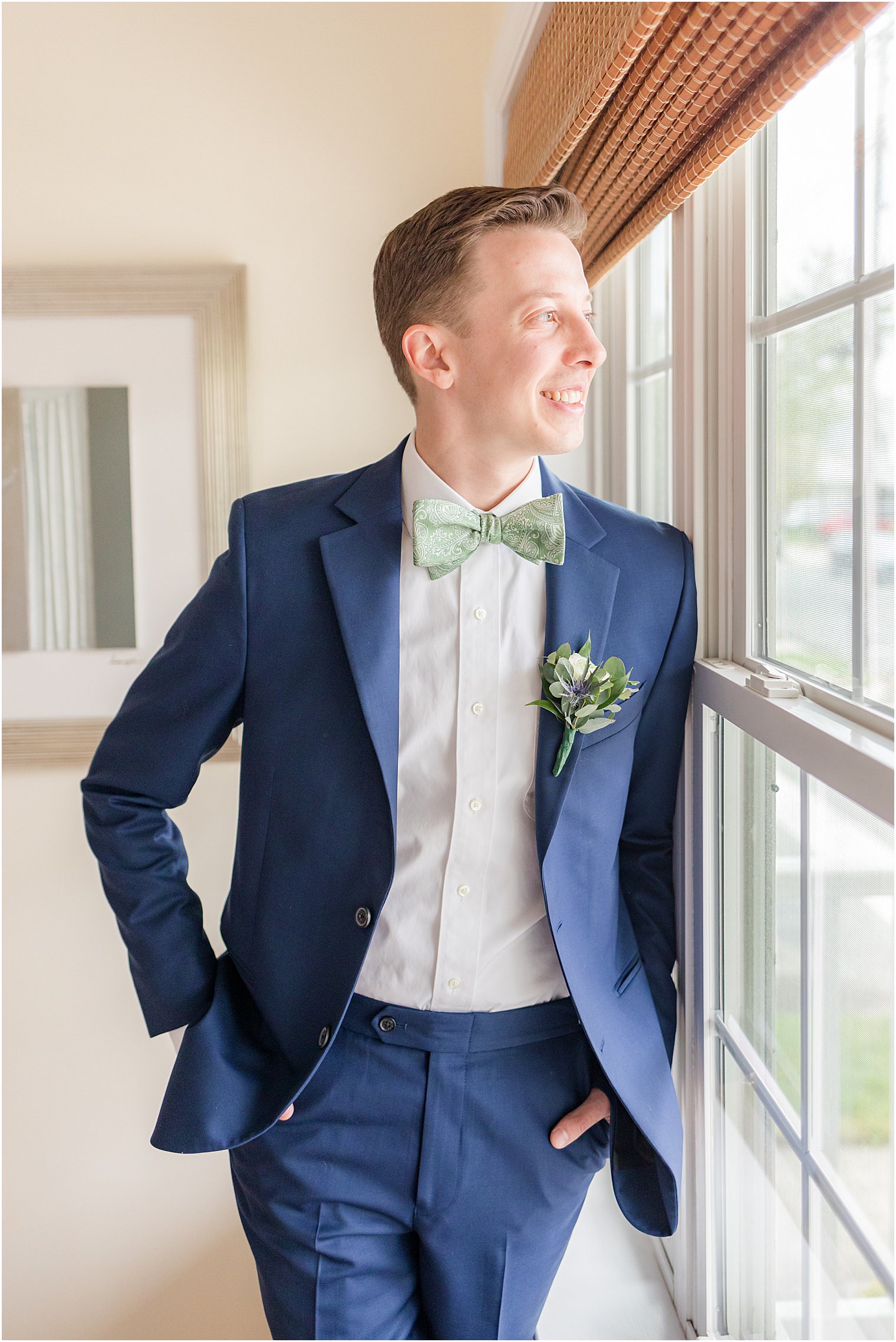 groom leans against window in navy suit