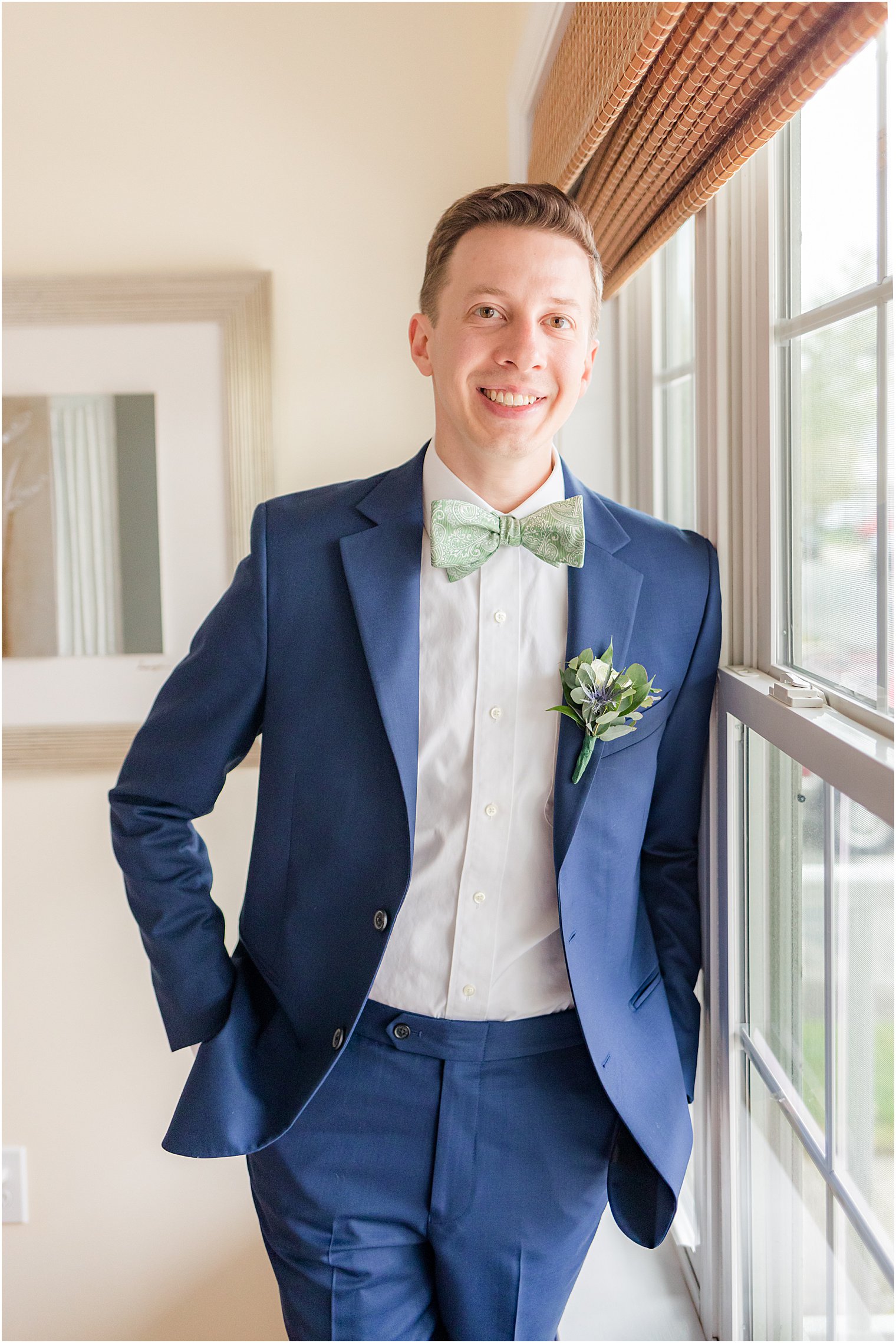 groom smiles leaning against window in navy suit
