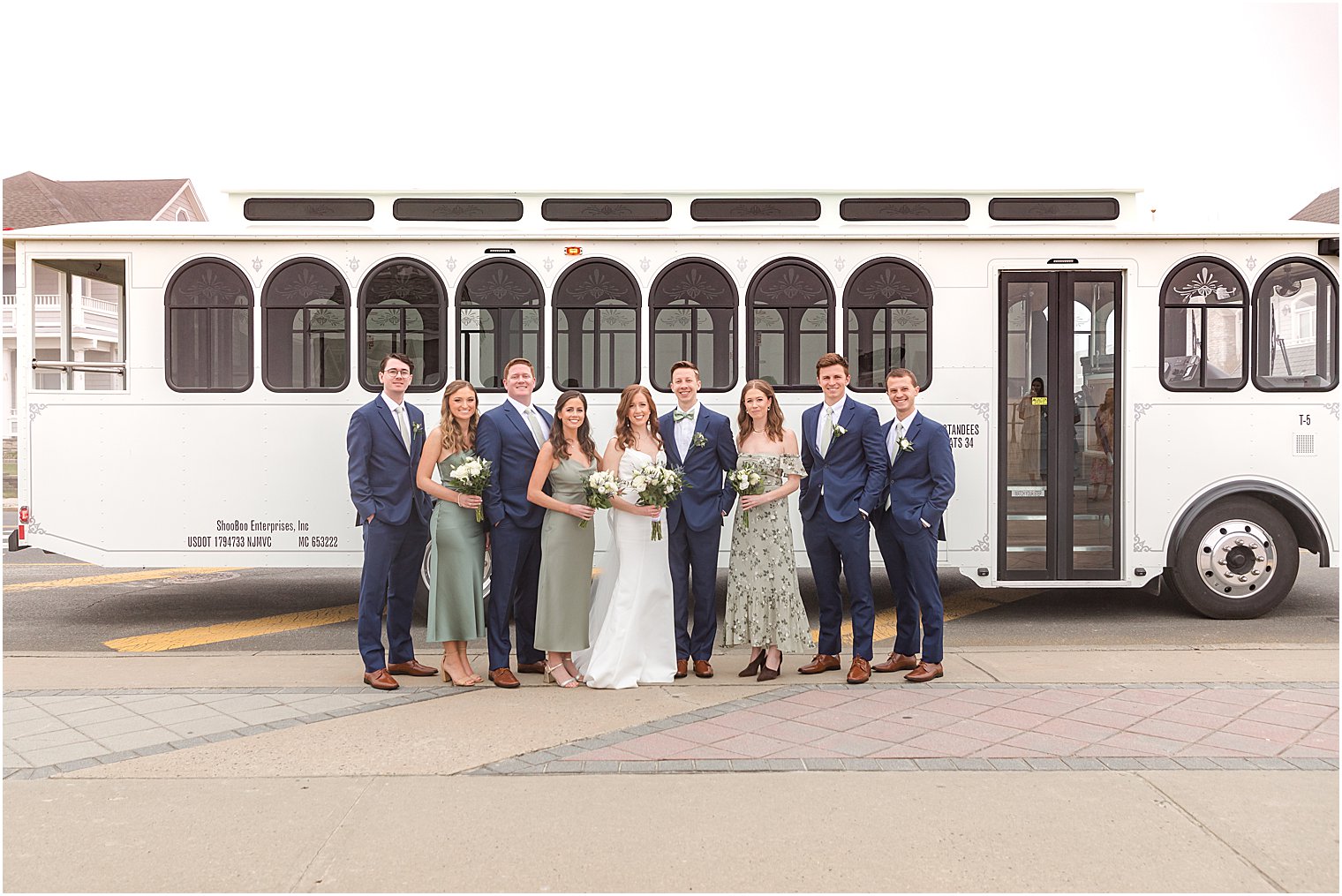 bride and groom stand with bridal party outside white trolley