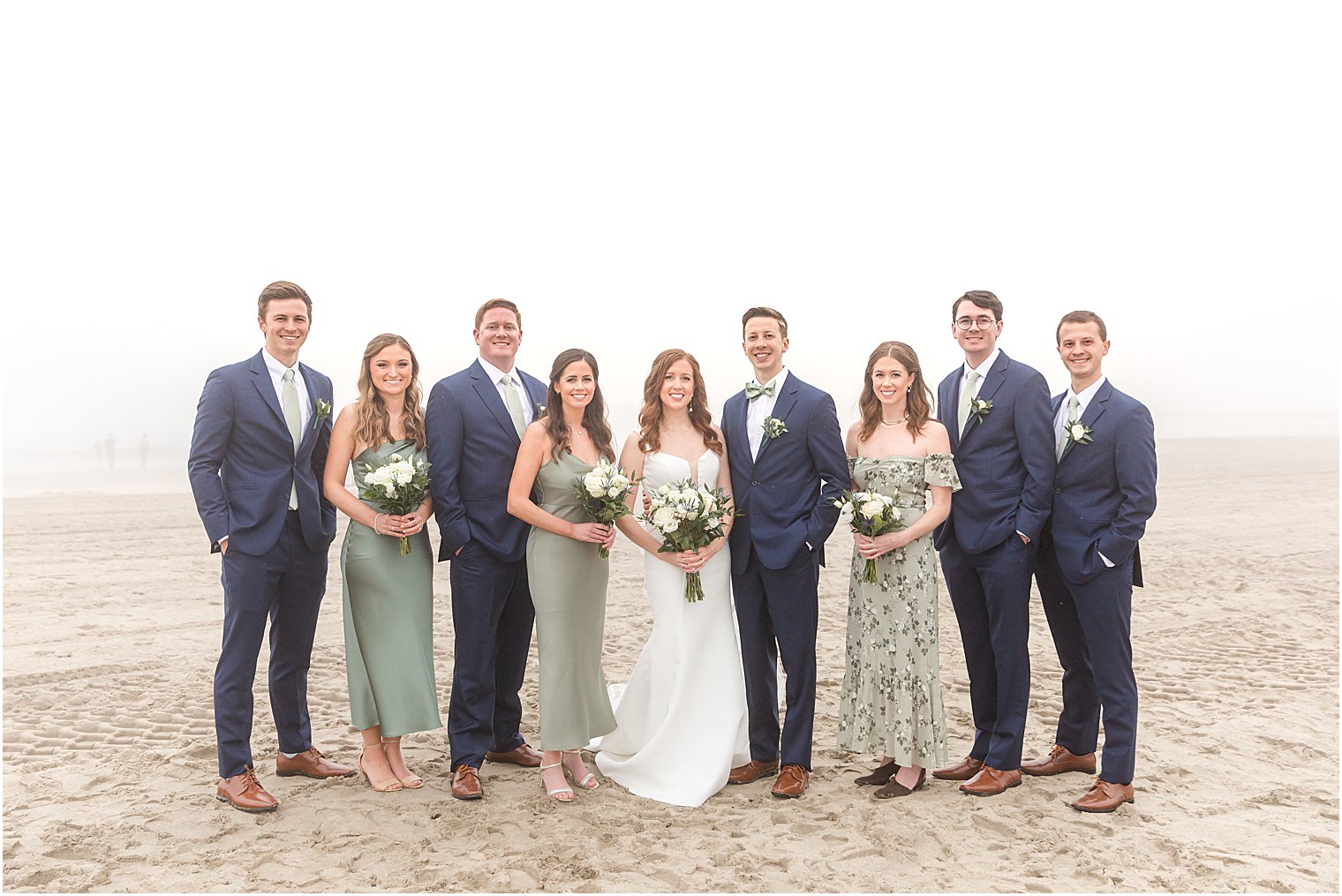 newlyweds stand on beach with bridal party