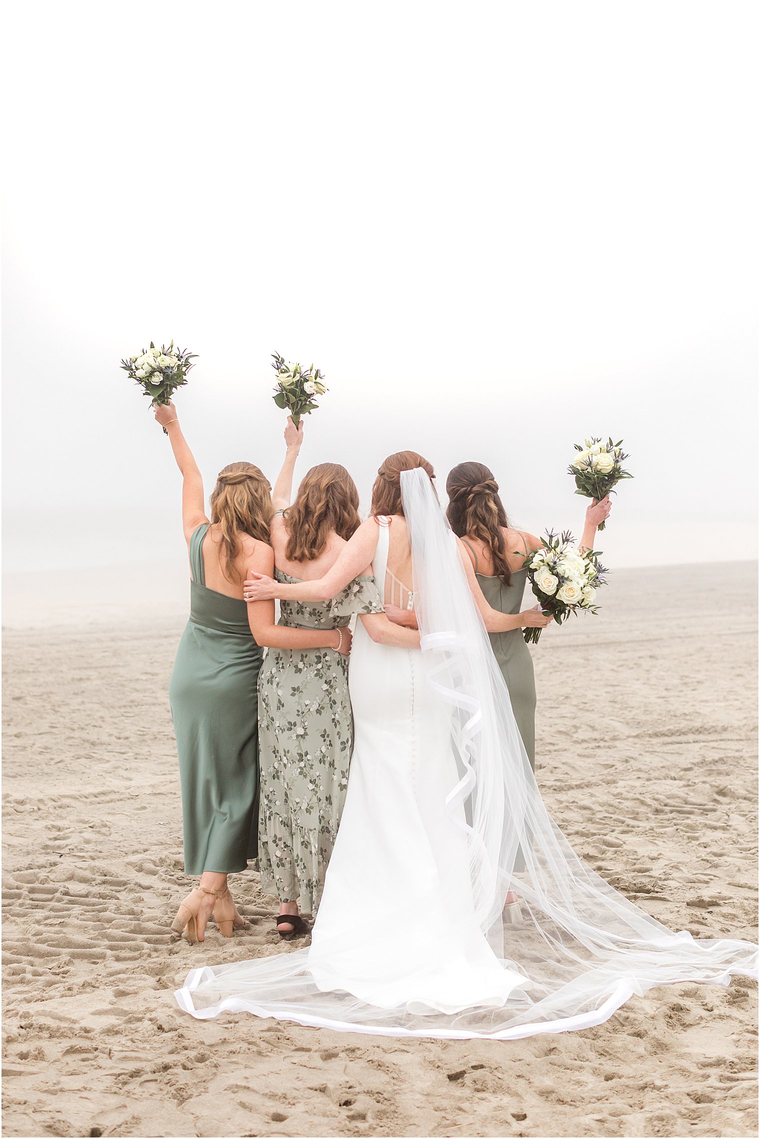 bride and bridesmaids hug on beach with bouquets in air