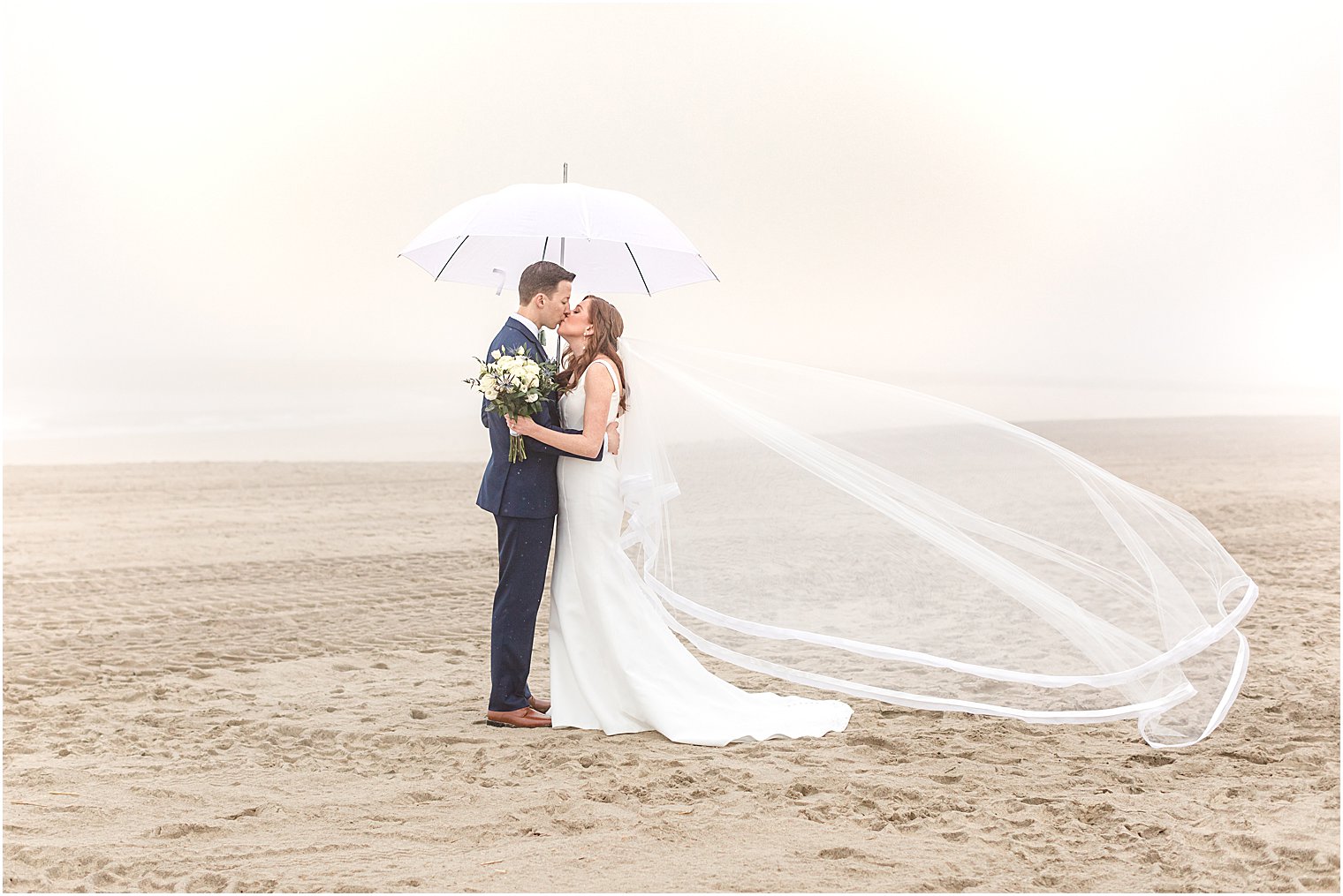 bride and groom pose under umbrella on beach