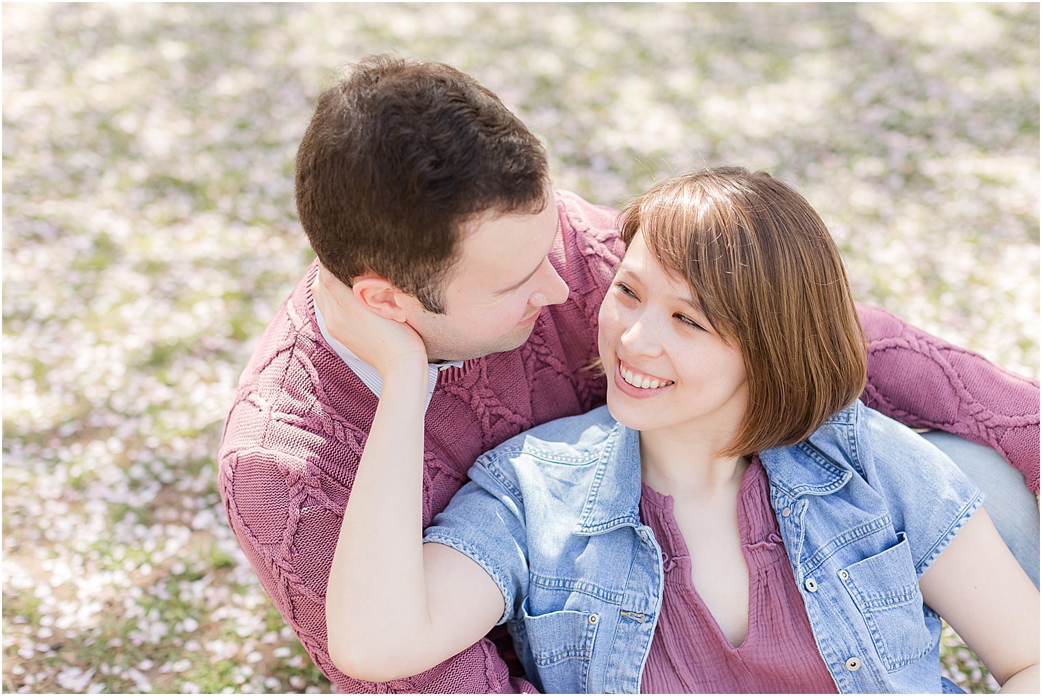 woman sits in front of man leaning into him for spring cherry blossom portraits