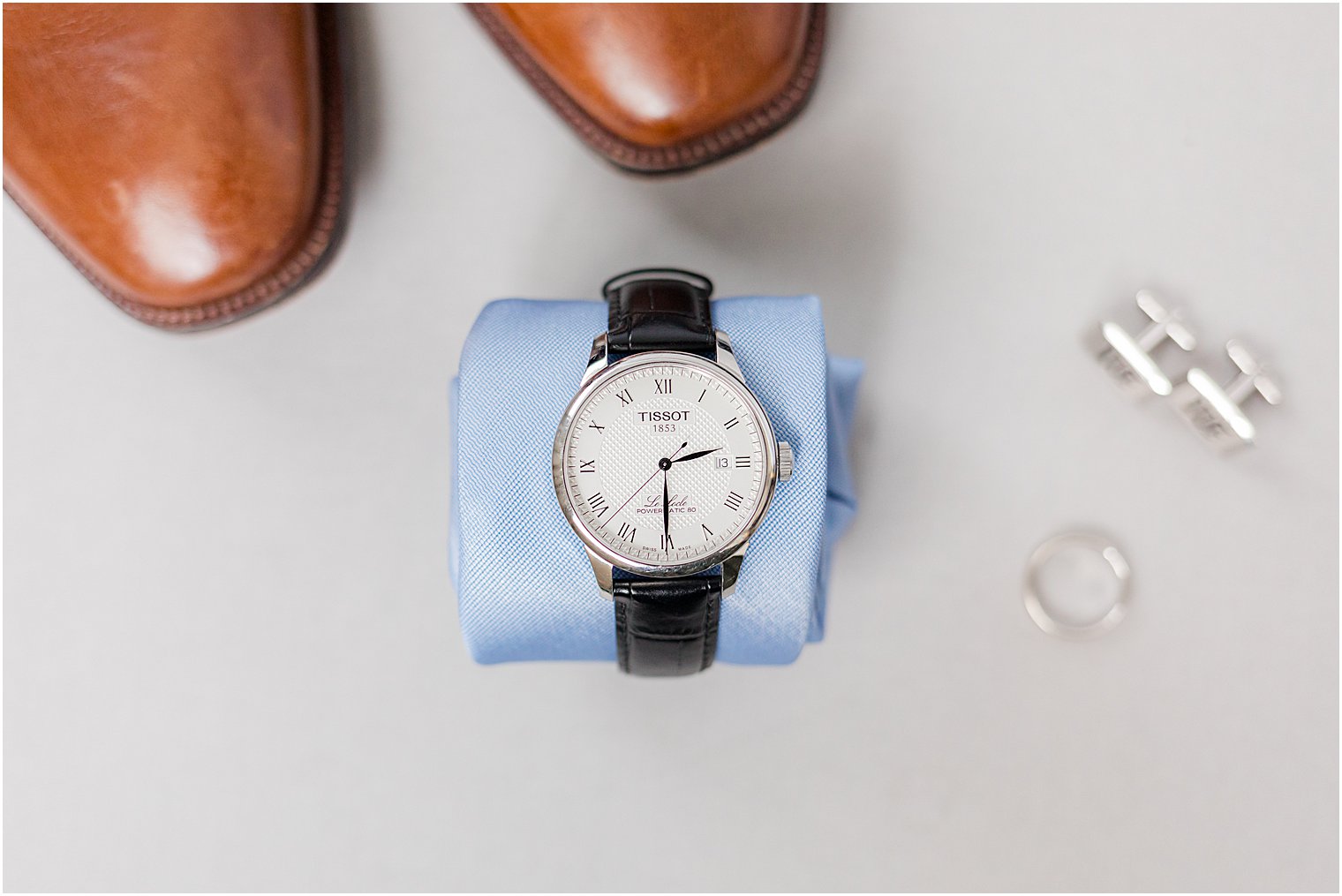 groom's watch lays on rolled up blue tie