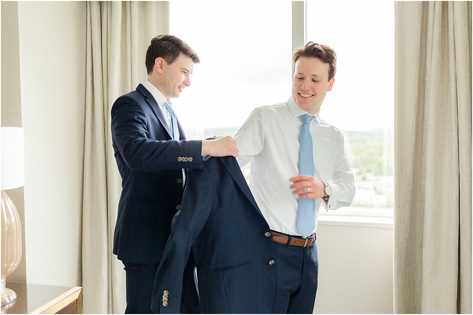 groomsman helps groom into coat jacket 