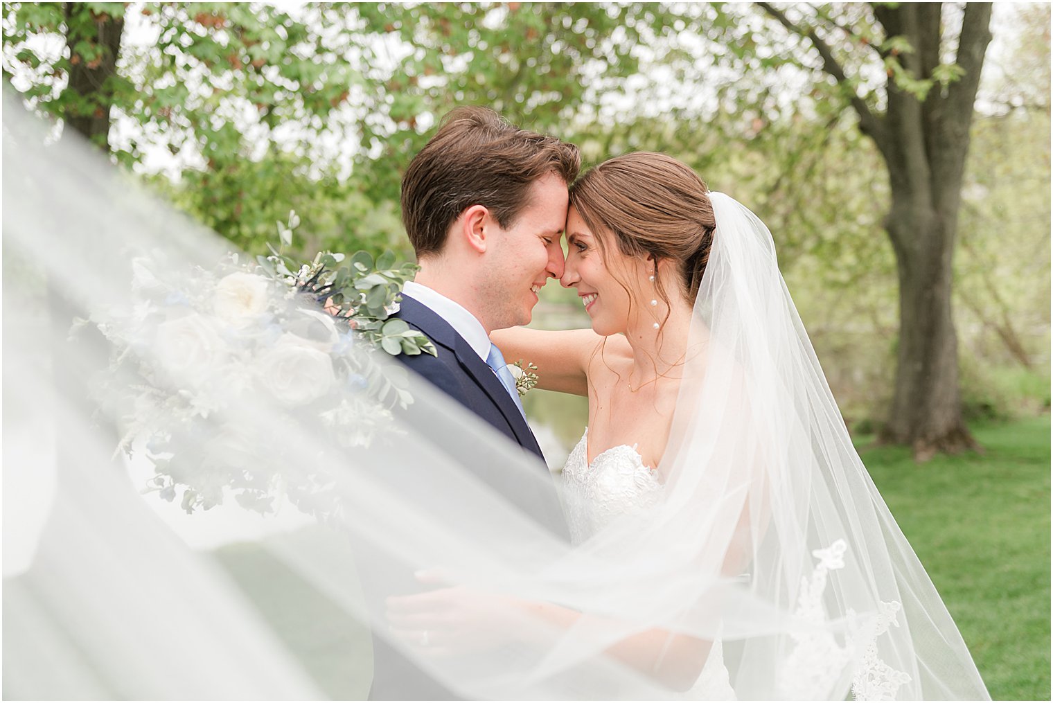 bride and groom touch foreheads while veil wraps around them