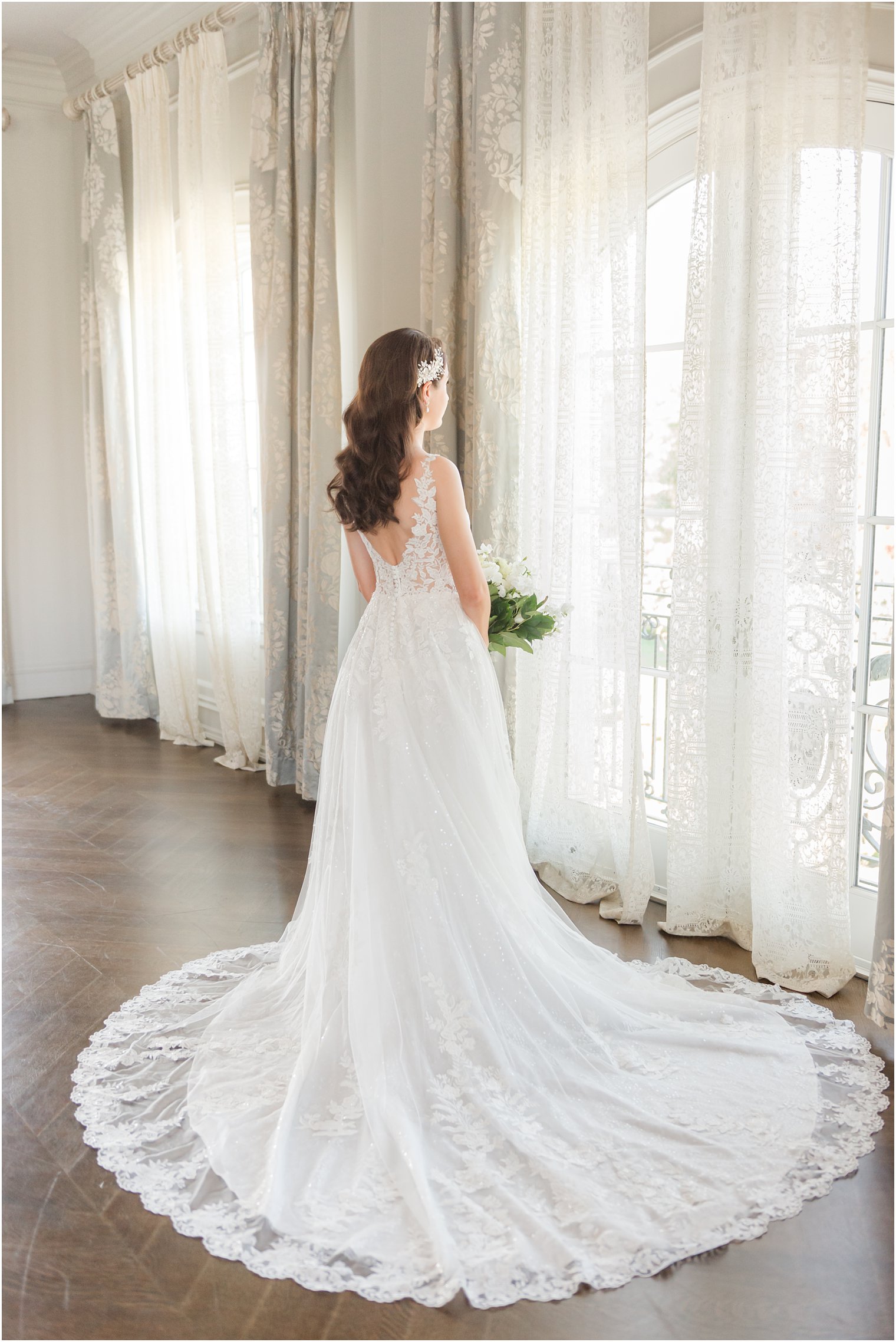 bride stands by window in bridal suite of Park Chateau Estate with dress draped around her