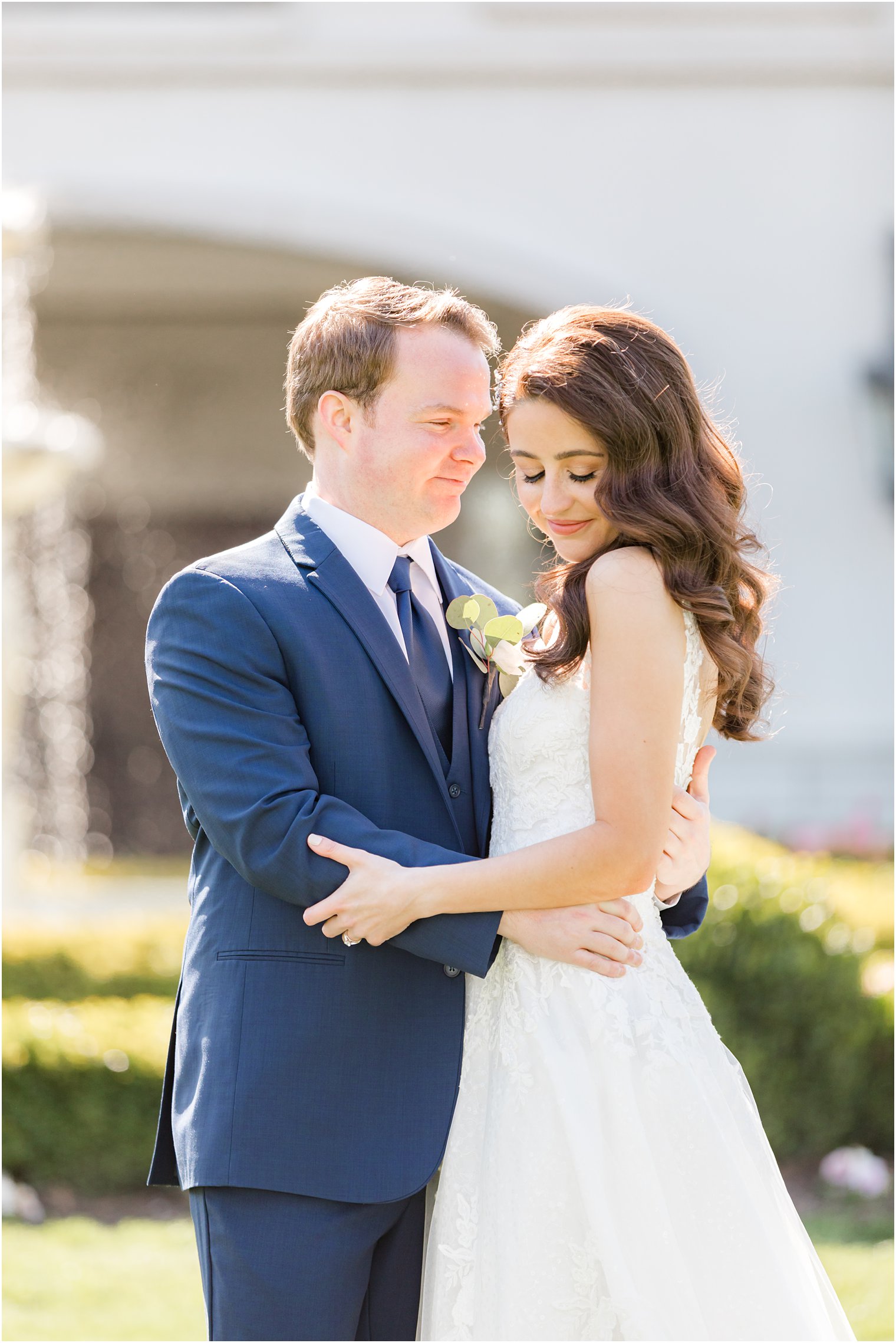 bride and groom hug close on lawn near fountain during NJ wedding photos